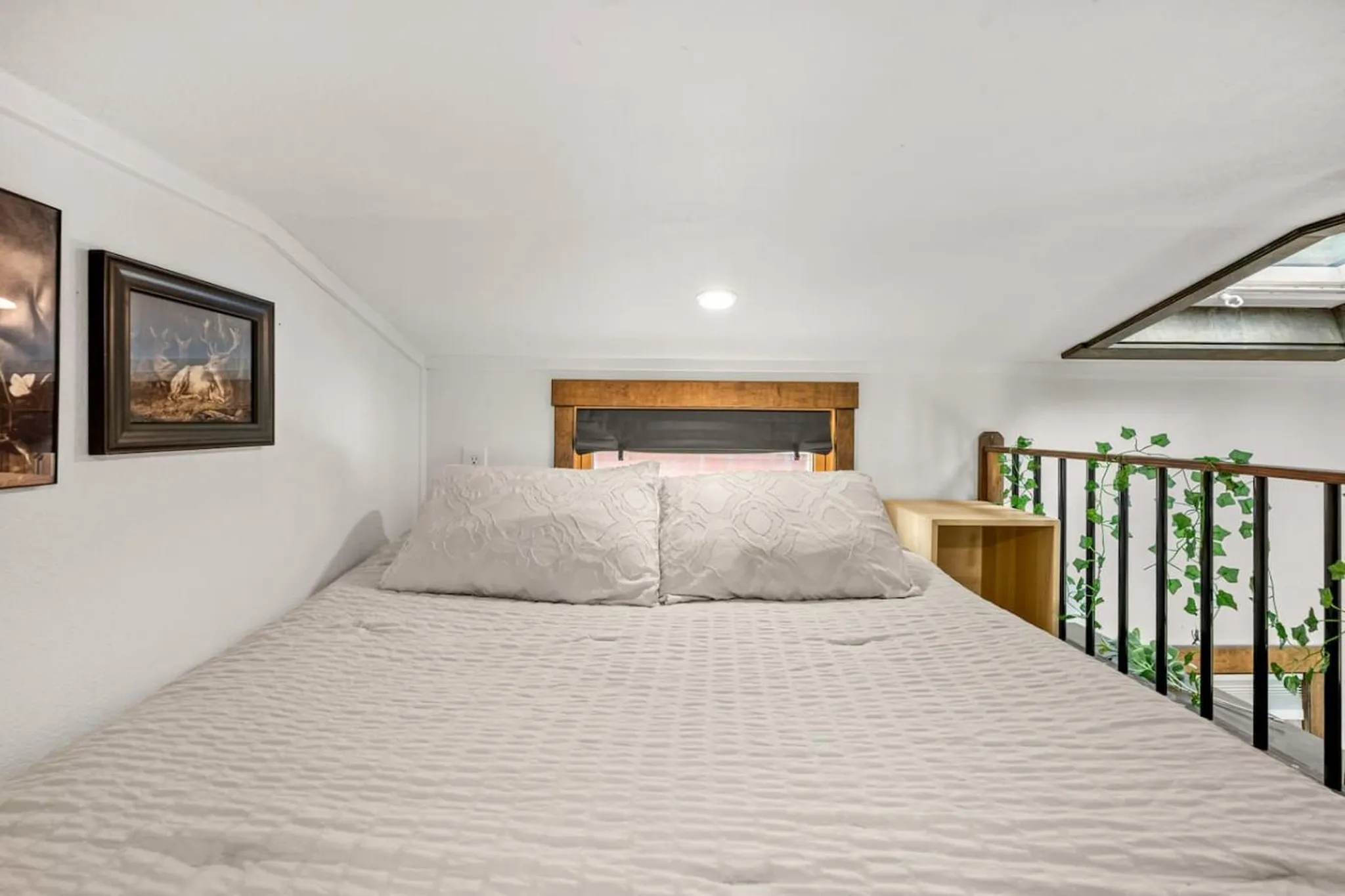 A cozy loft bedroom with a large bed, a window, and decorative ivy.