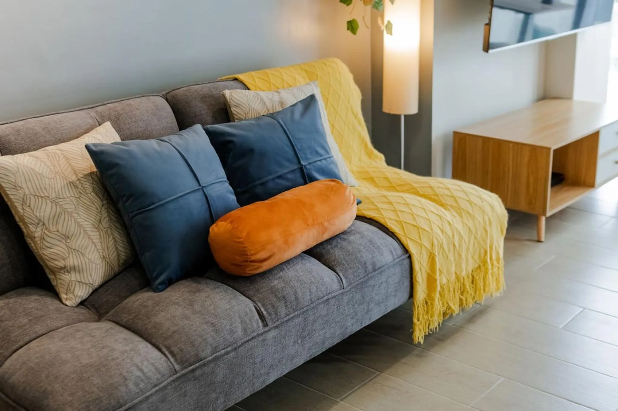 A grey sofa with blue, orange and patterned pillows, and a yellow throw.