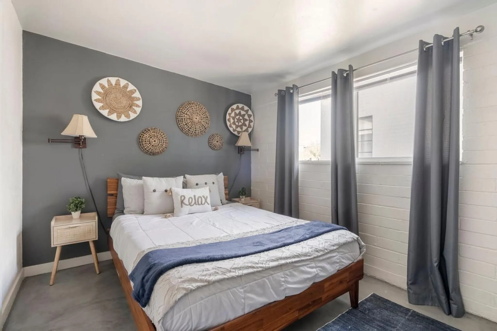 A cozy bedroom with a queen-size bed, dark grey walls, and natural woven wall decor.