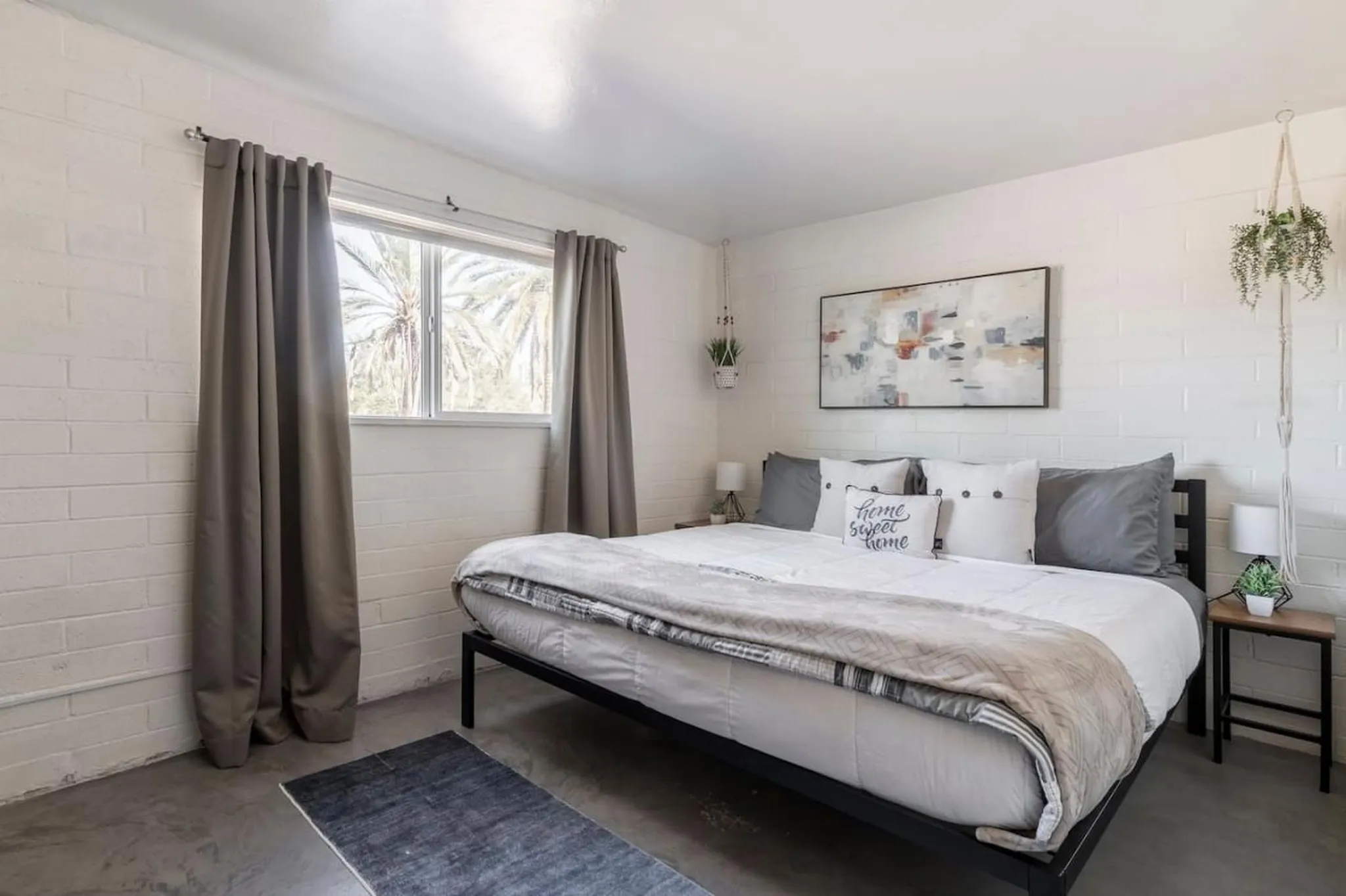 A modern bedroom with a black metal bed frame, white bedding, and a large abstract painting.