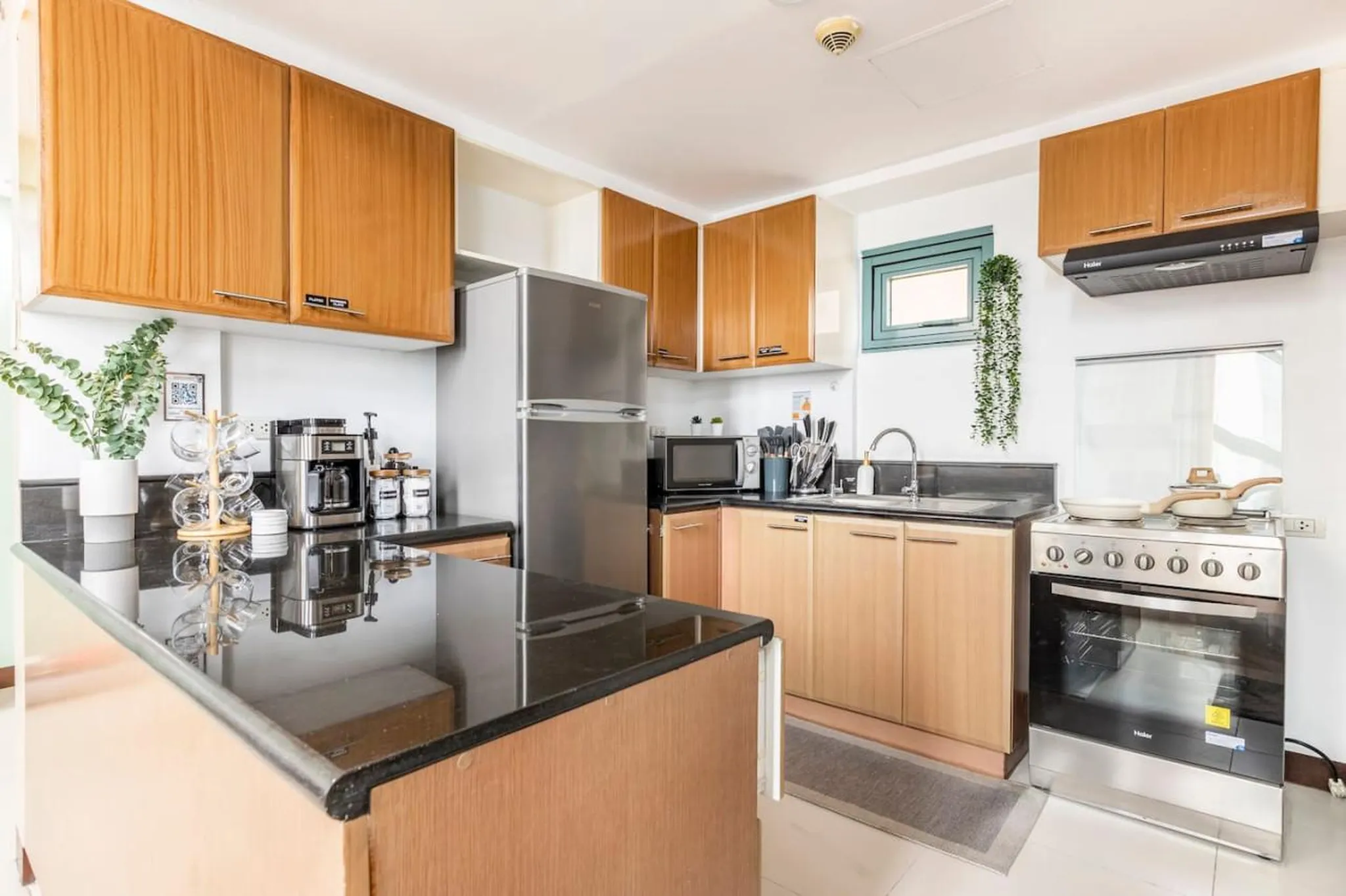 A modern kitchen with light wood cabinets, stainless steel appliances, and black countertops.