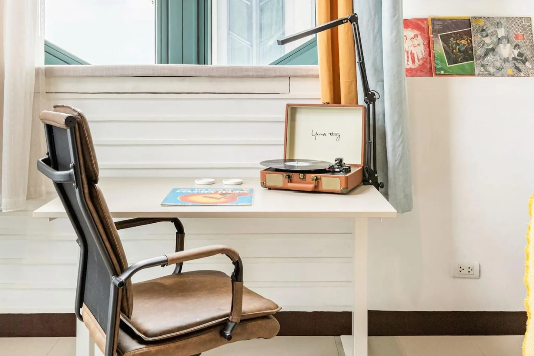 A vintage record player sits on a desk with a record on it, next to a brown leather chair.
