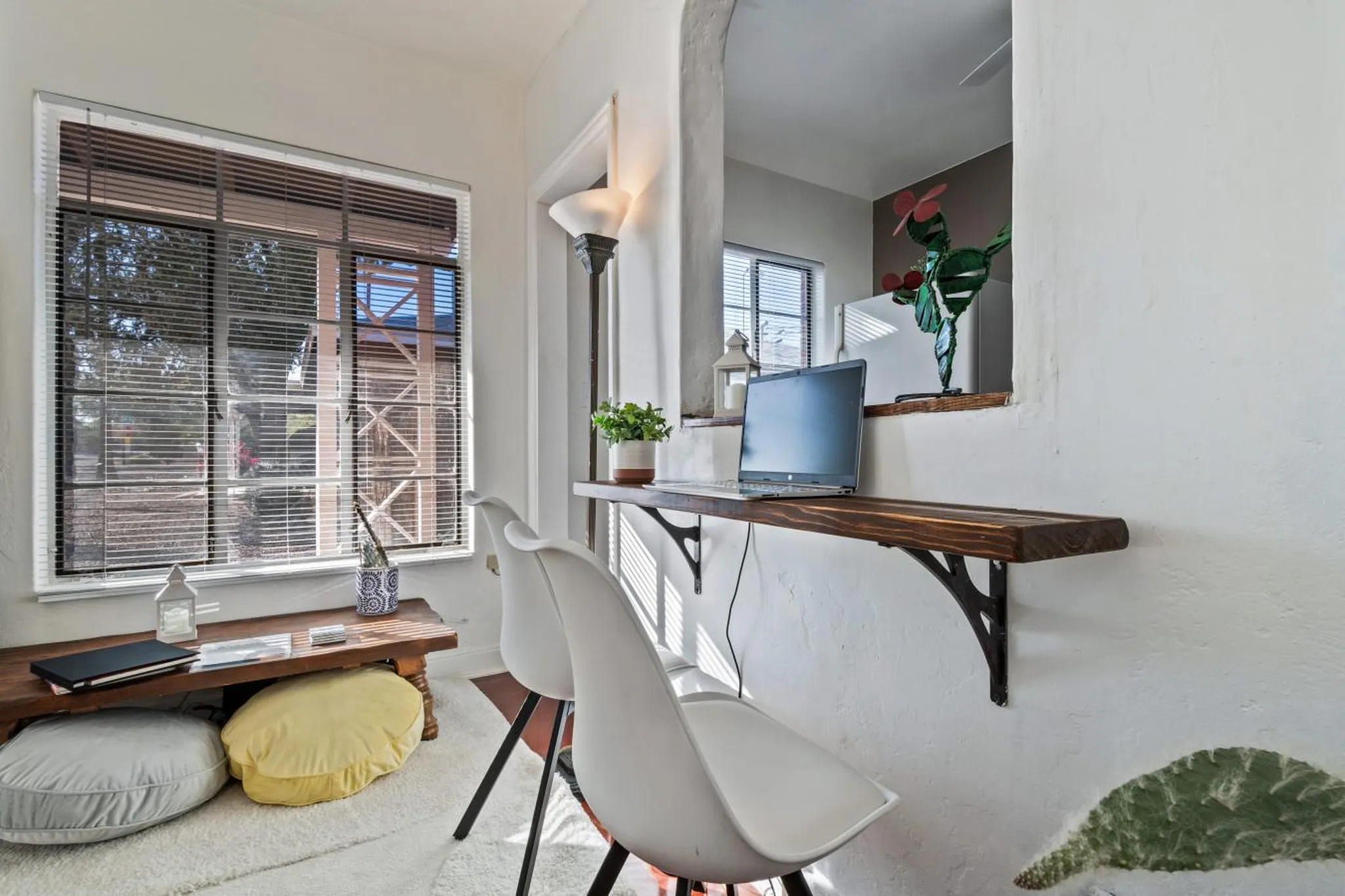 A workspace with a laptop and chair, next to a window and a decorative cactus.