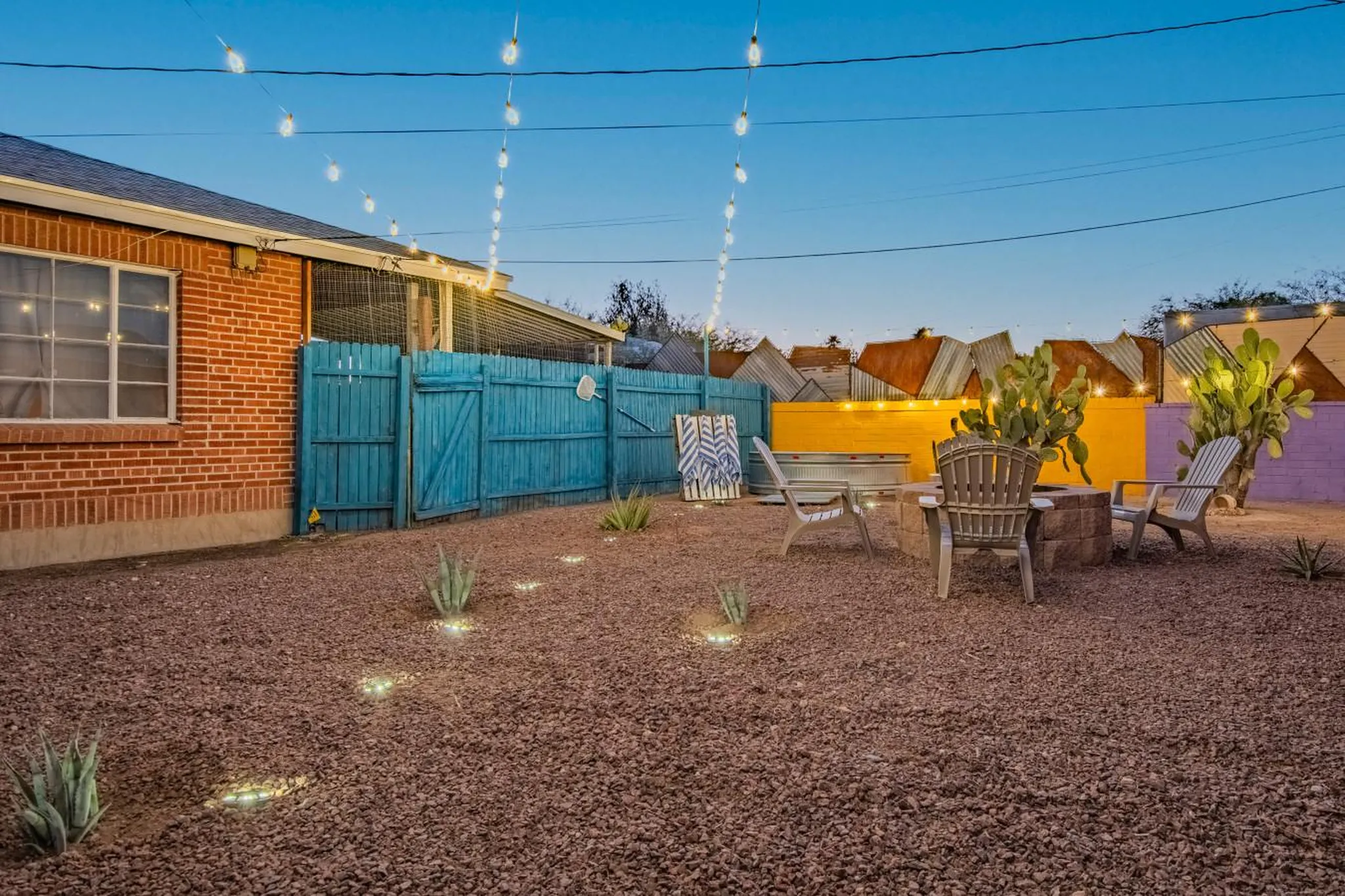 A backyard patio with a fire pit, chairs, and string lights.
