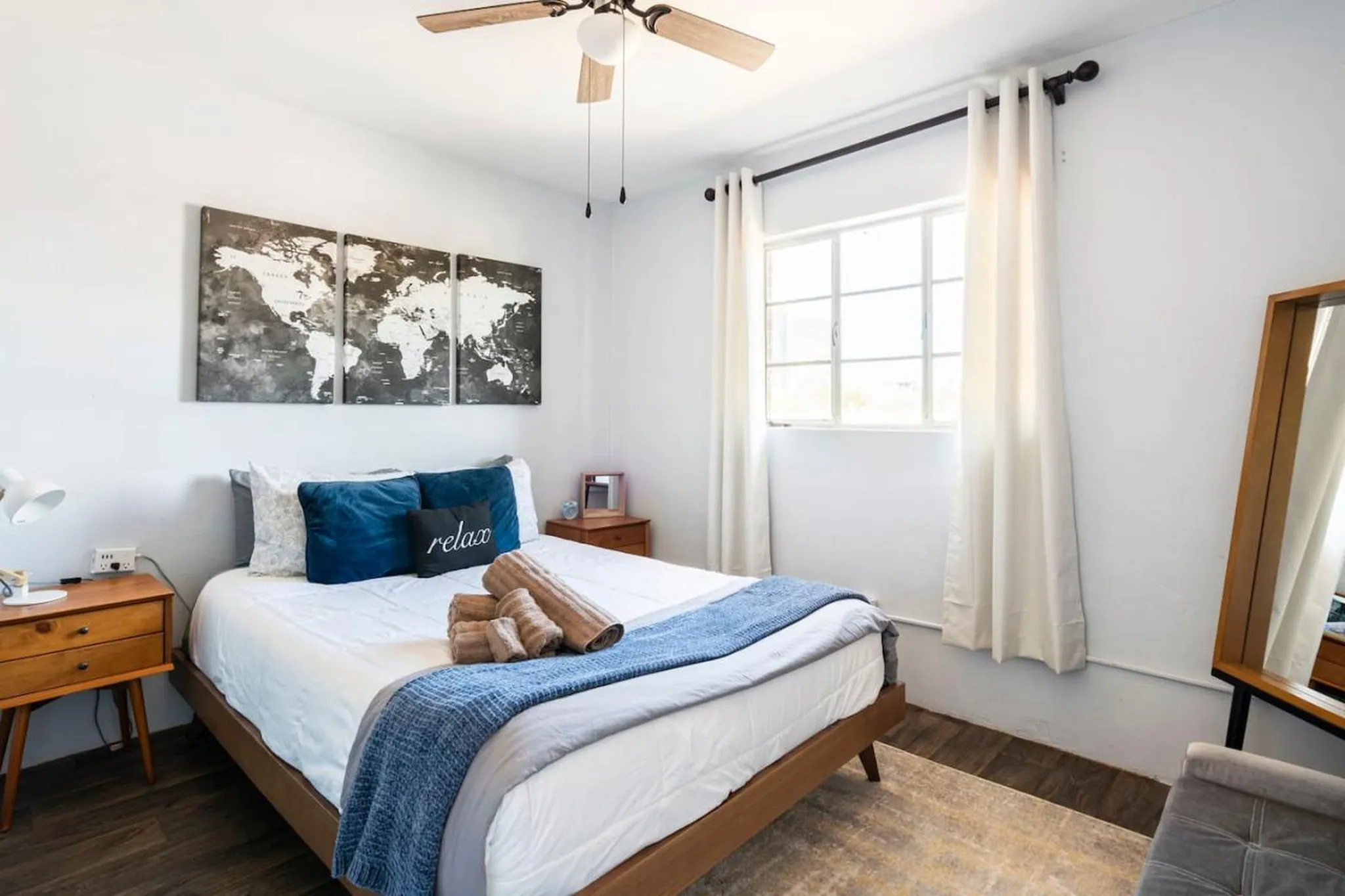 A bedroom with a bed, a window with white curtains, and a world map on the wall.