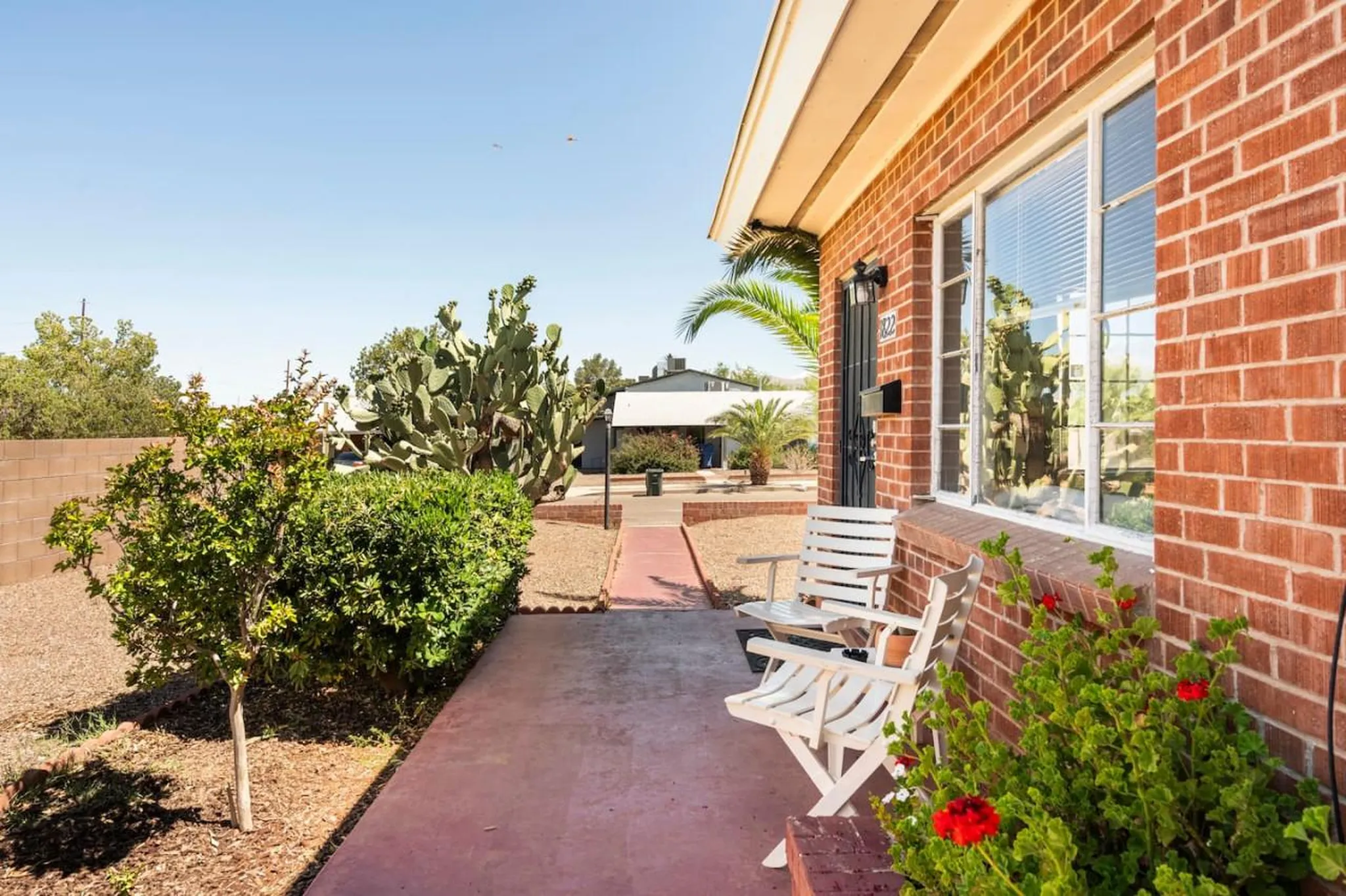 A residential doorway with red brick, a white bench and blooming red flowers.