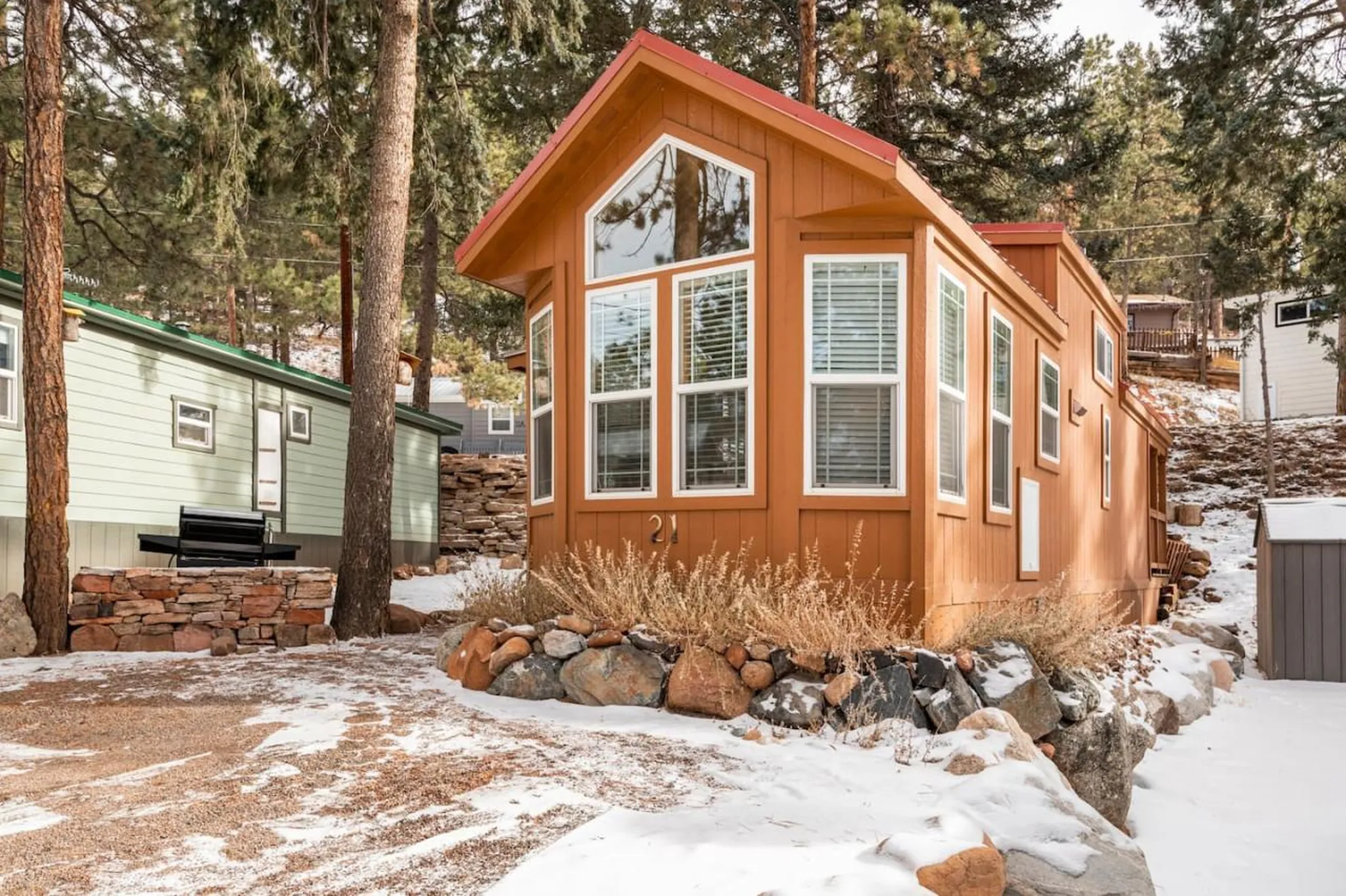 A charming orange tiny home with a red roof sits in a snowy wooded area.