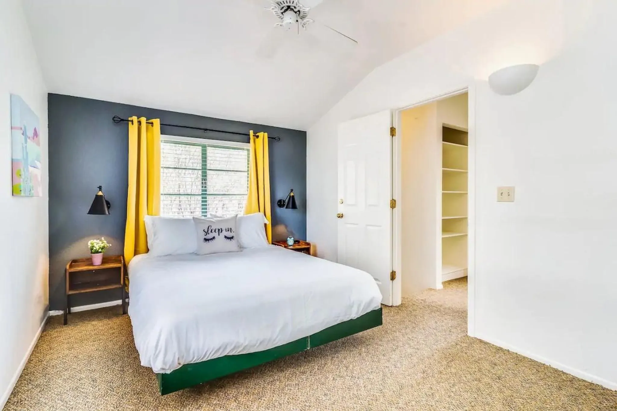 A cozy bedroom with a dark gray wall, yellow curtains, and a white bed.