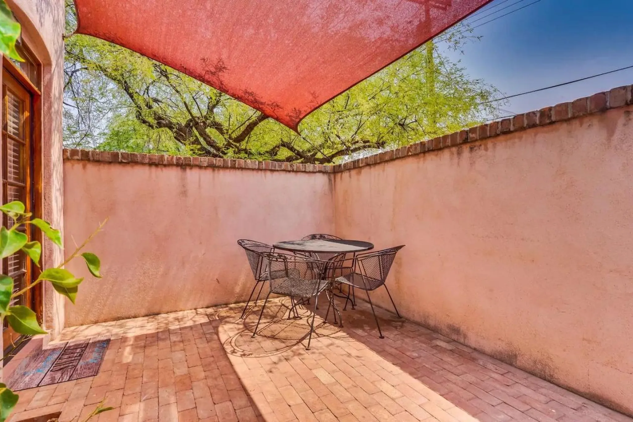 A pink stucco courtyard with a wrought iron table and chairs under a red canopy.