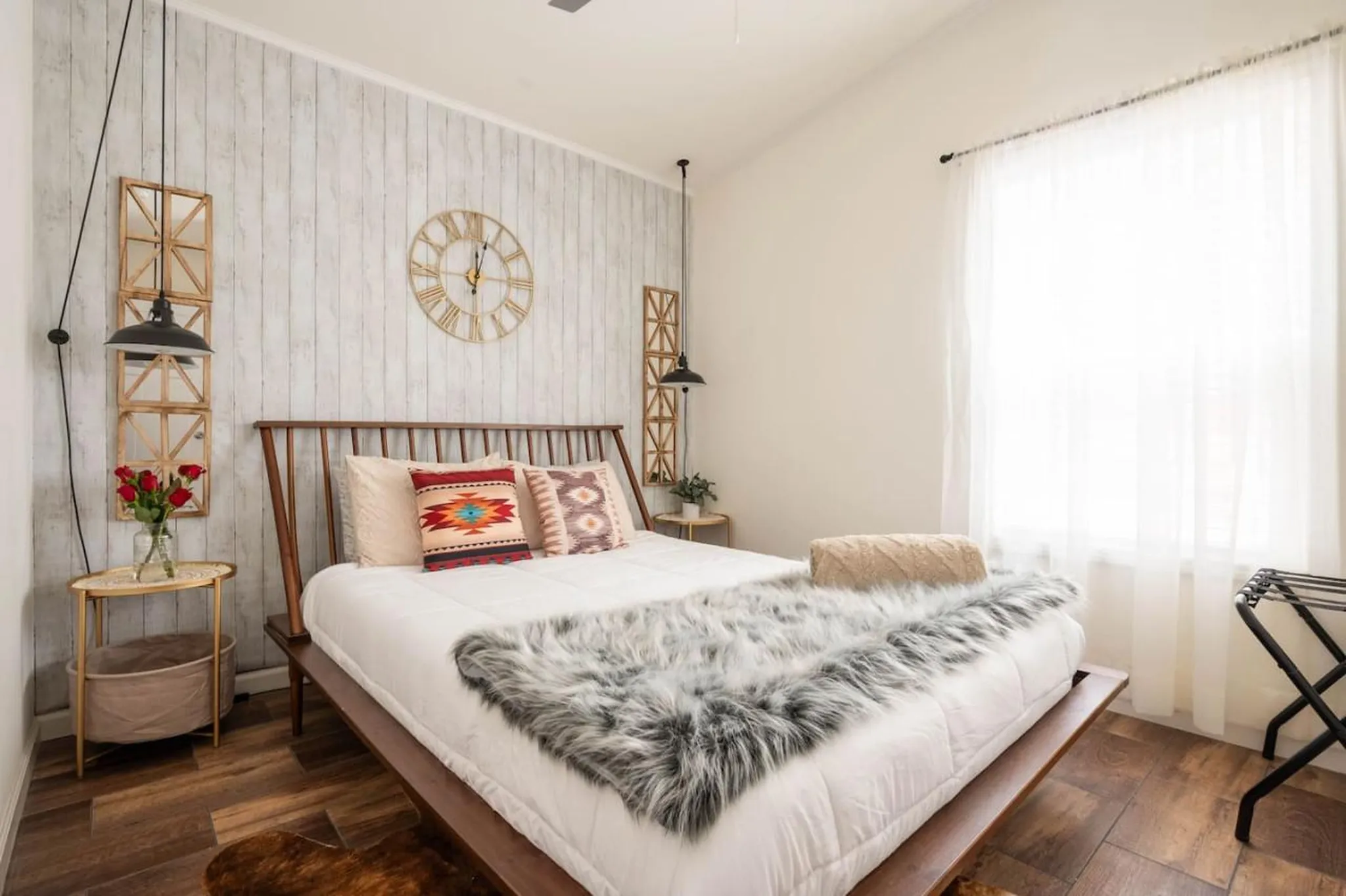 A stylish bedroom featuring a wooden bed with patterned pillows and a faux fur throw.
