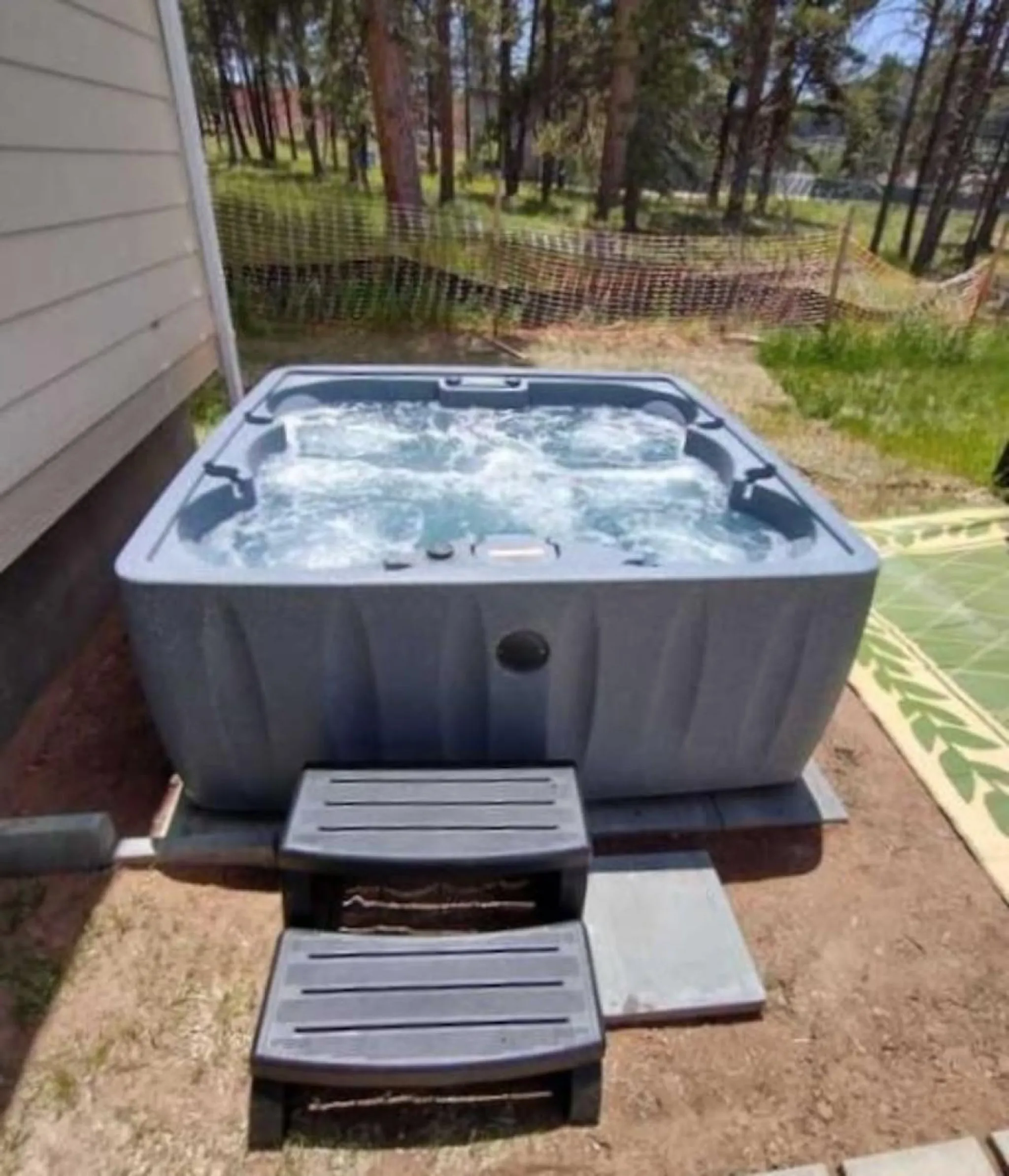 A gray hot tub with bubbling water is next to a house. Two gray steps lead up to it.