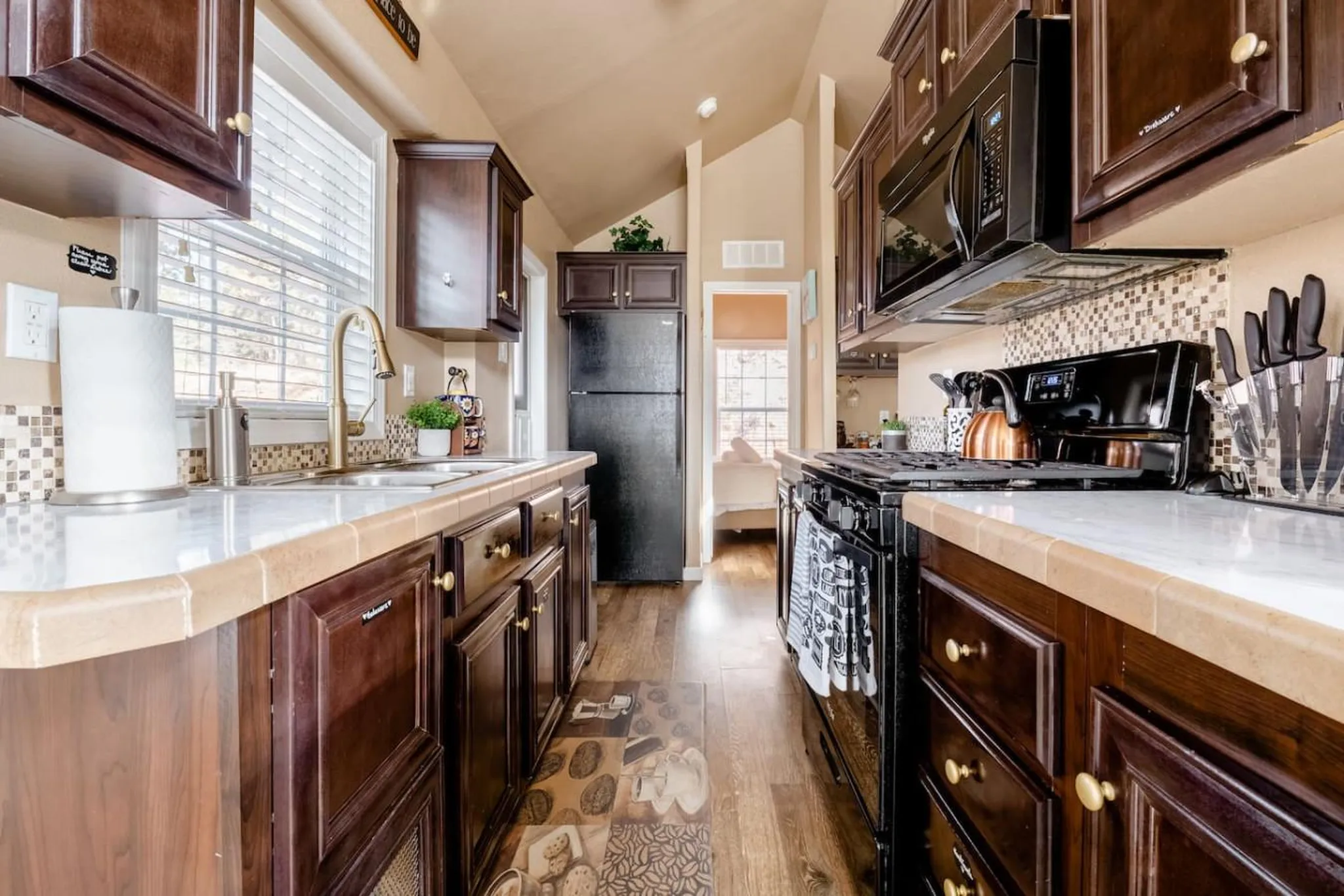 A small, charming kitchen with dark wood cabinets, a black stove, and a beige ceiling.