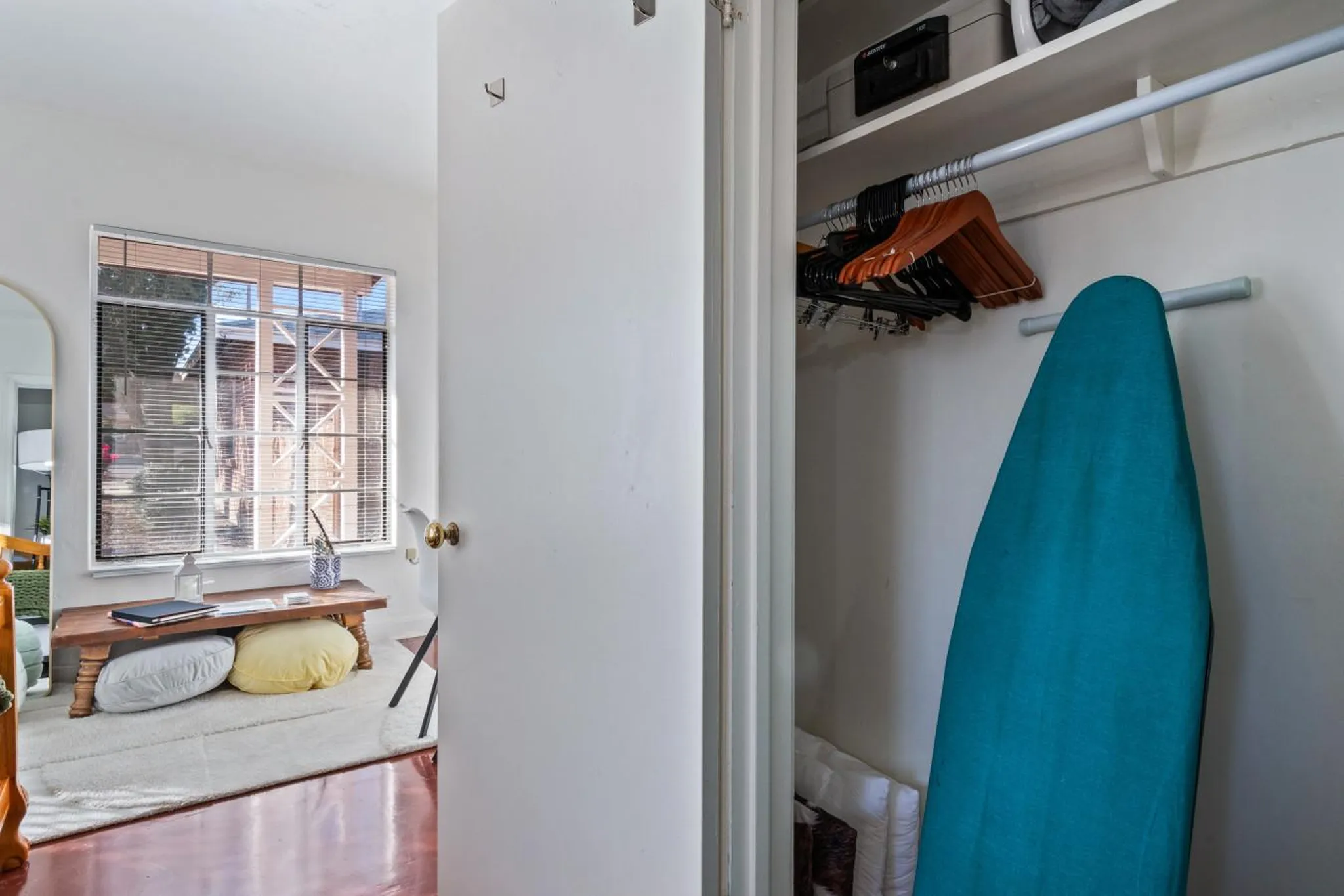 A closet with an ironing board, clothes hangers, and a safe.