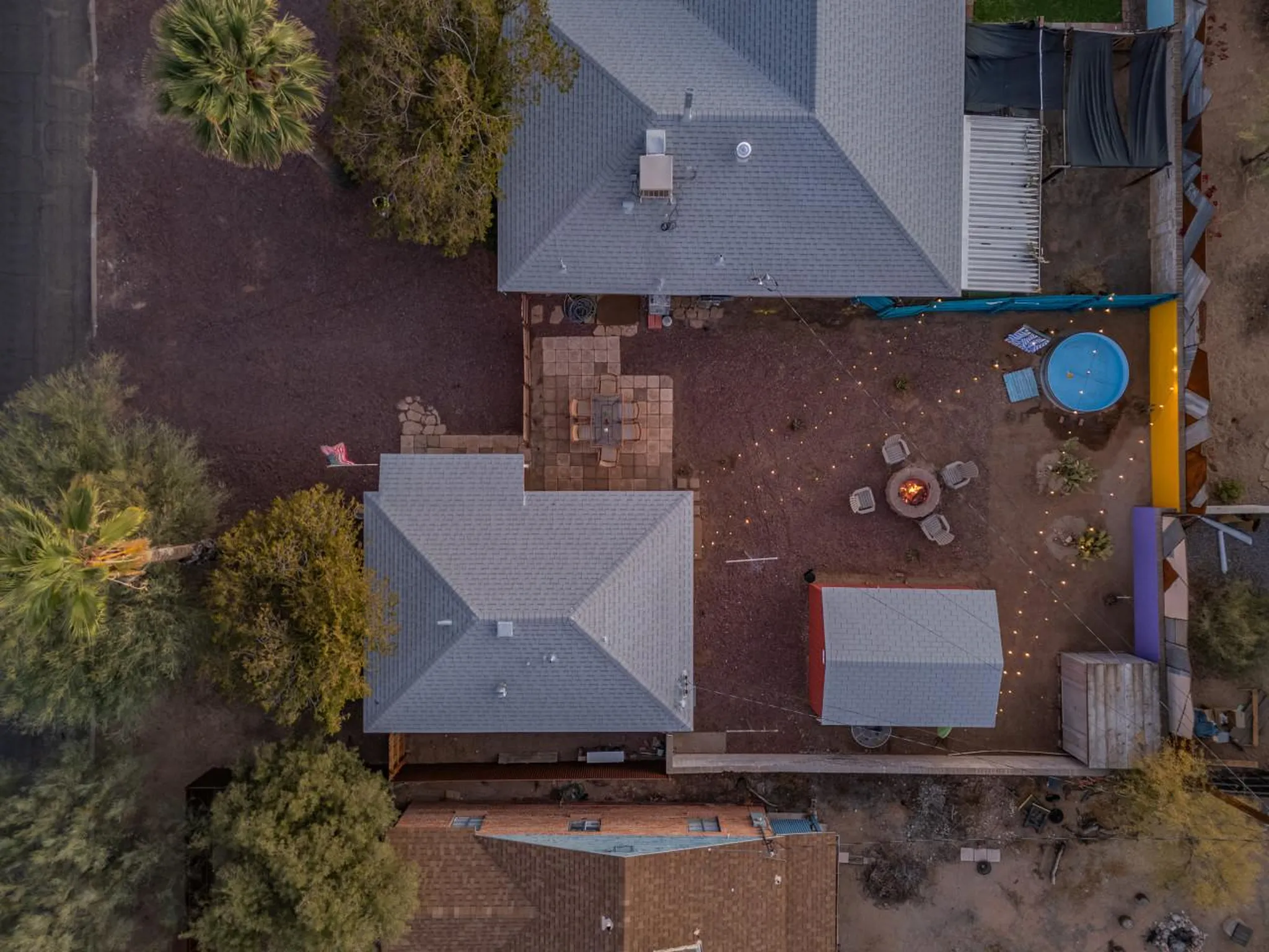 An aerial view of a backyard with a fire pit, chairs, and a blue pool.
