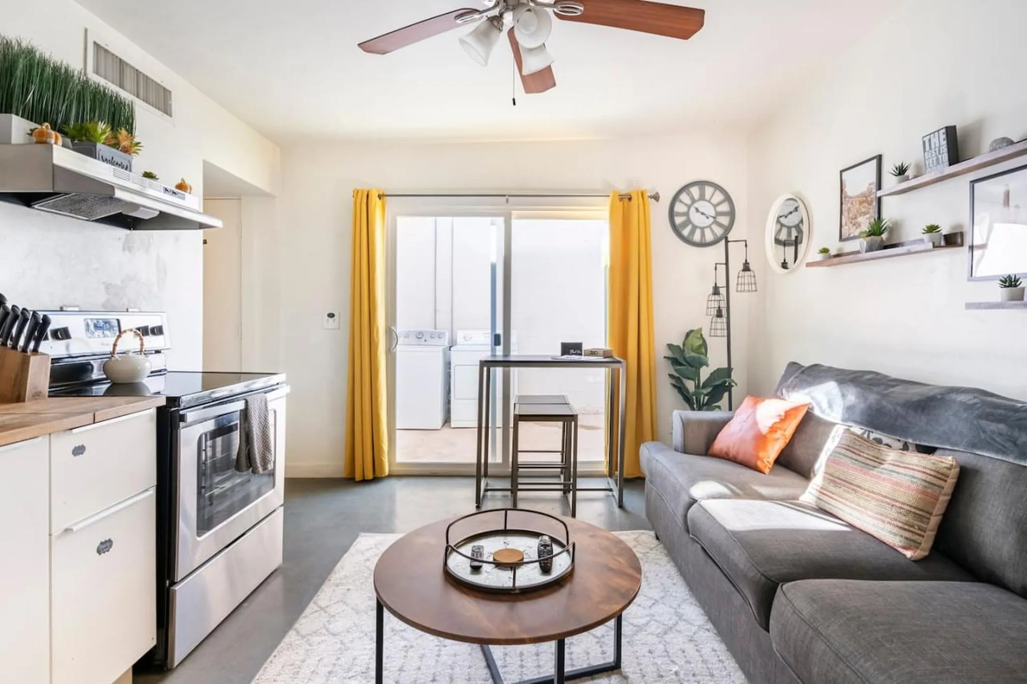 A stylish living room and kitchen with a gray sofa, coffee table, and kitchen appliances.