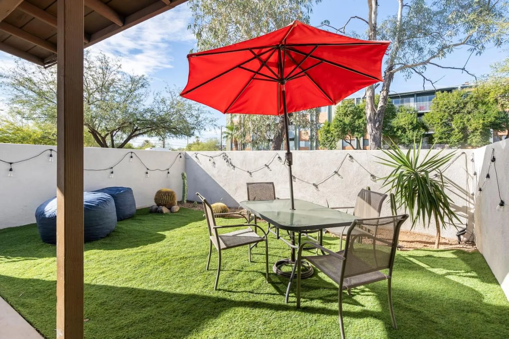 Backyard patio with artificial turf, a red umbrella, table and chairs, and two large beanbag chairs.