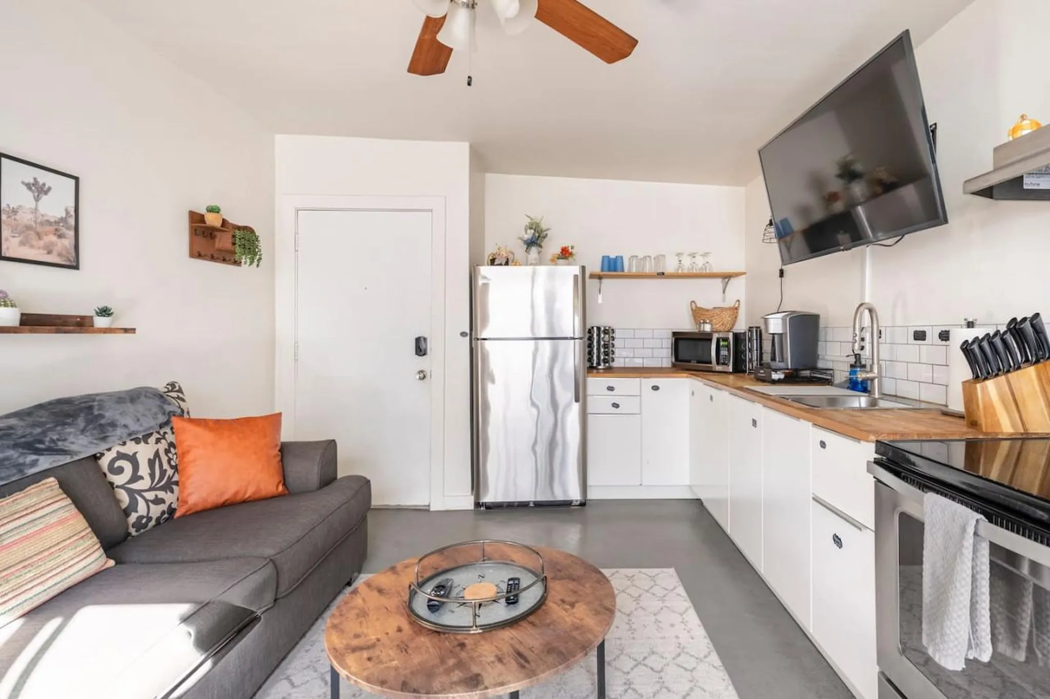 A bright kitchen and living area features a stainless steel refrigerator, modern cabinets, and a com