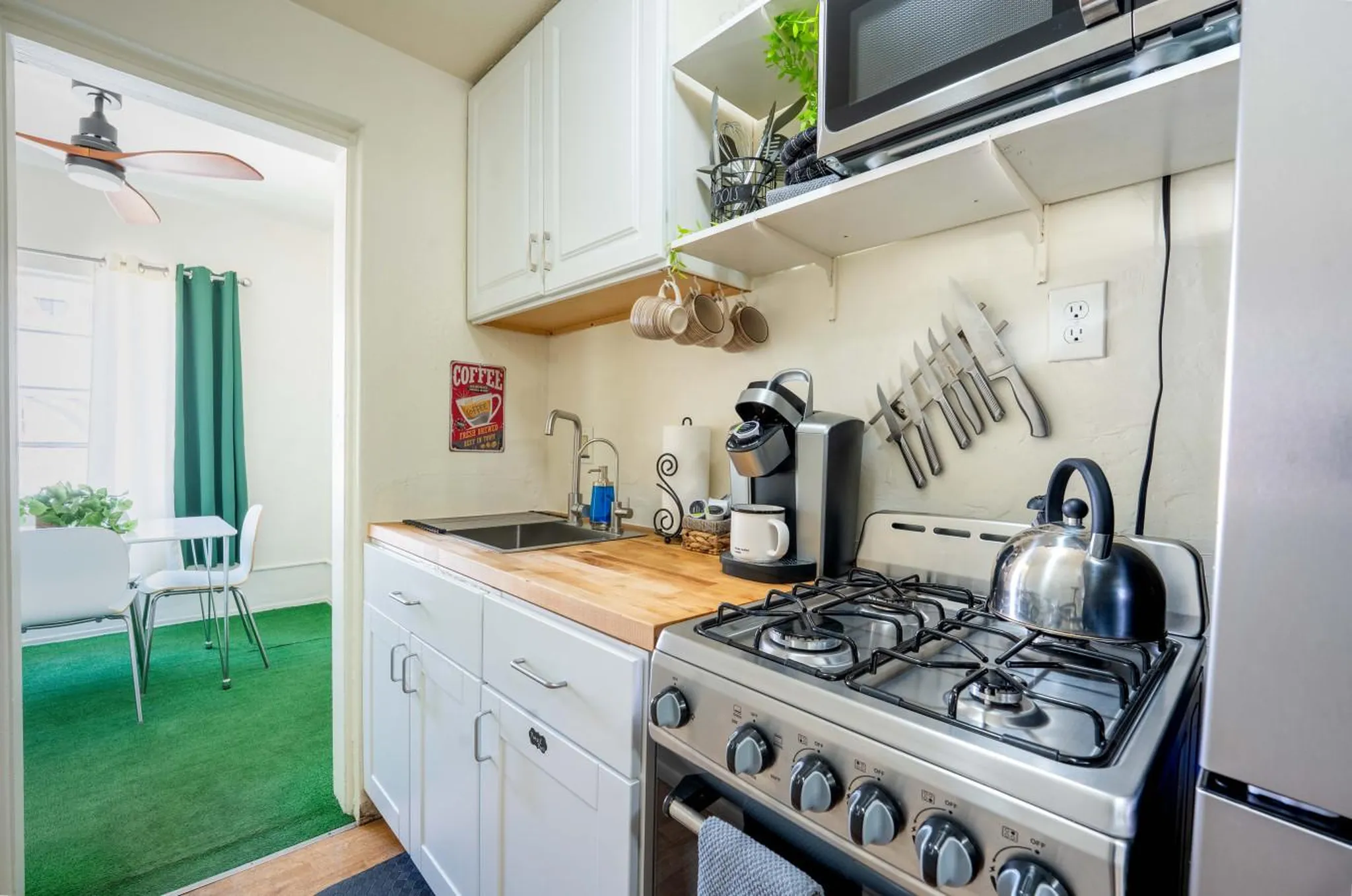 A cozy kitchen with a coffee maker, a kettle on a stove, and cabinets.