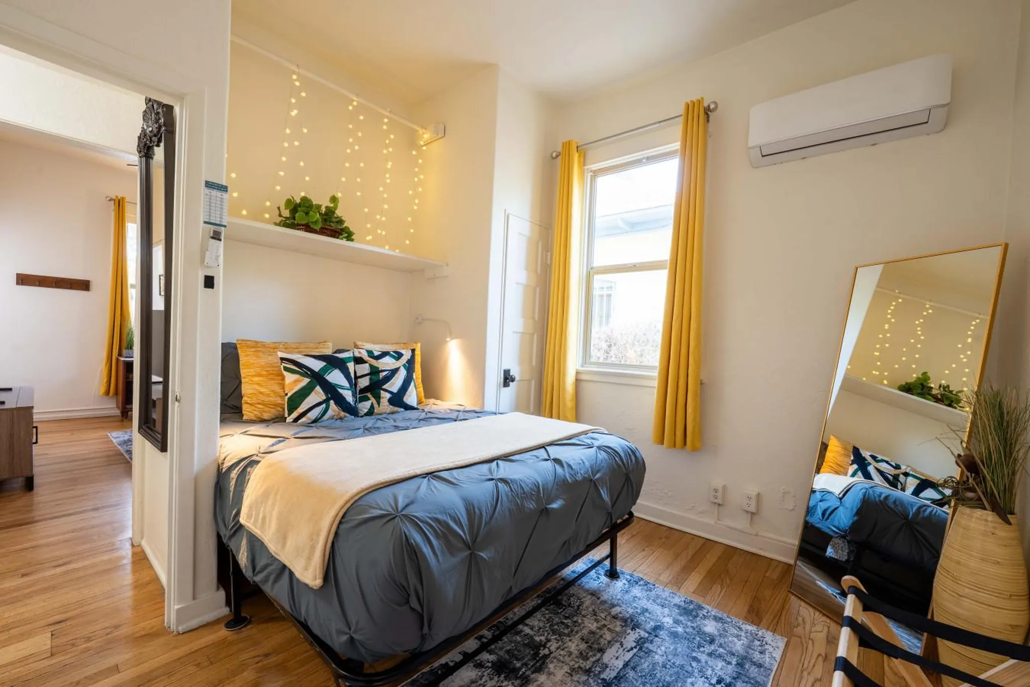 A cozy bedroom features a bed with blue comforter and decorative pillows, bedside lights, and yellow