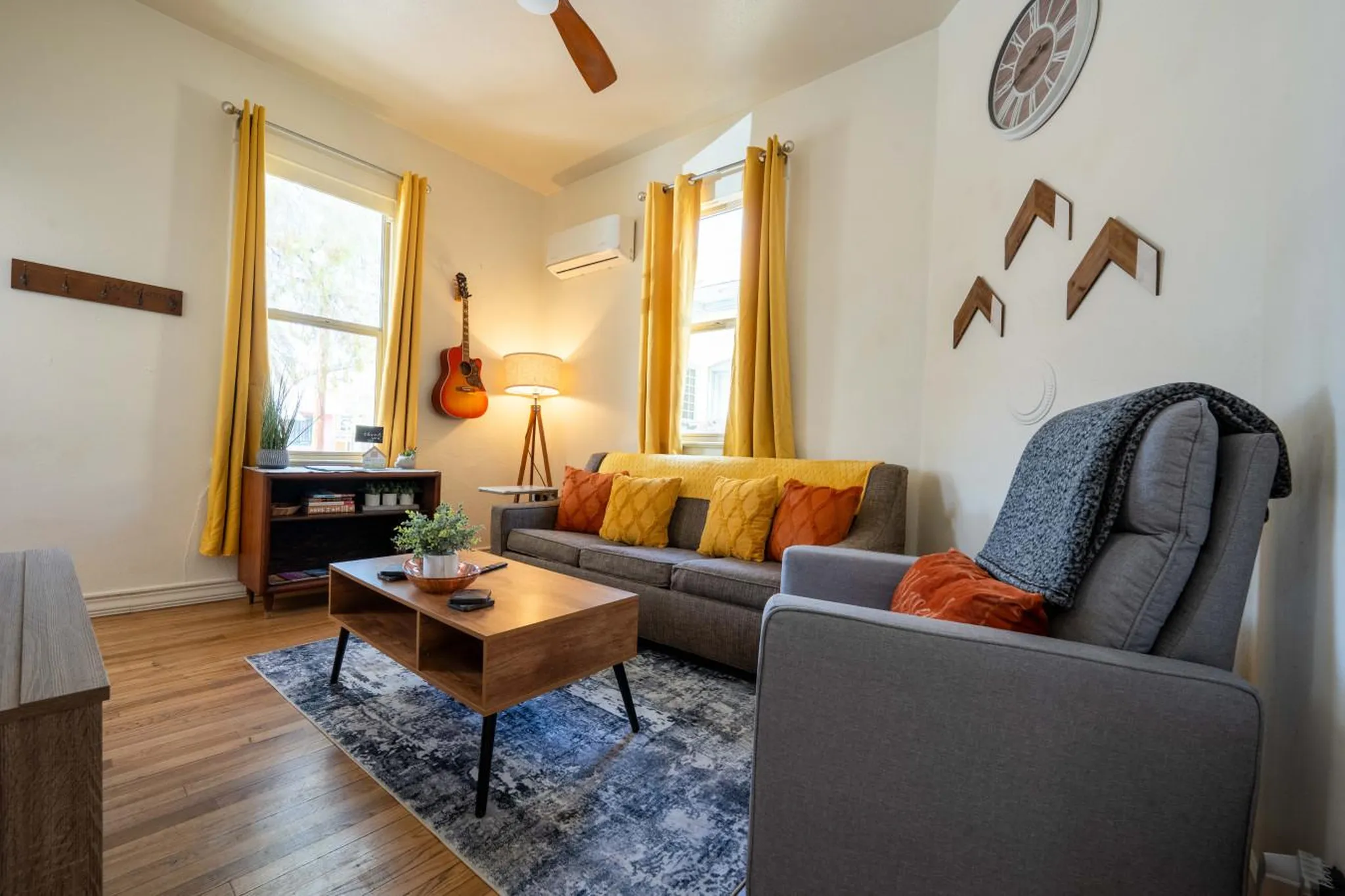A living room with a gray sofa, wooden coffee table, and a guitar hanging on the wall.