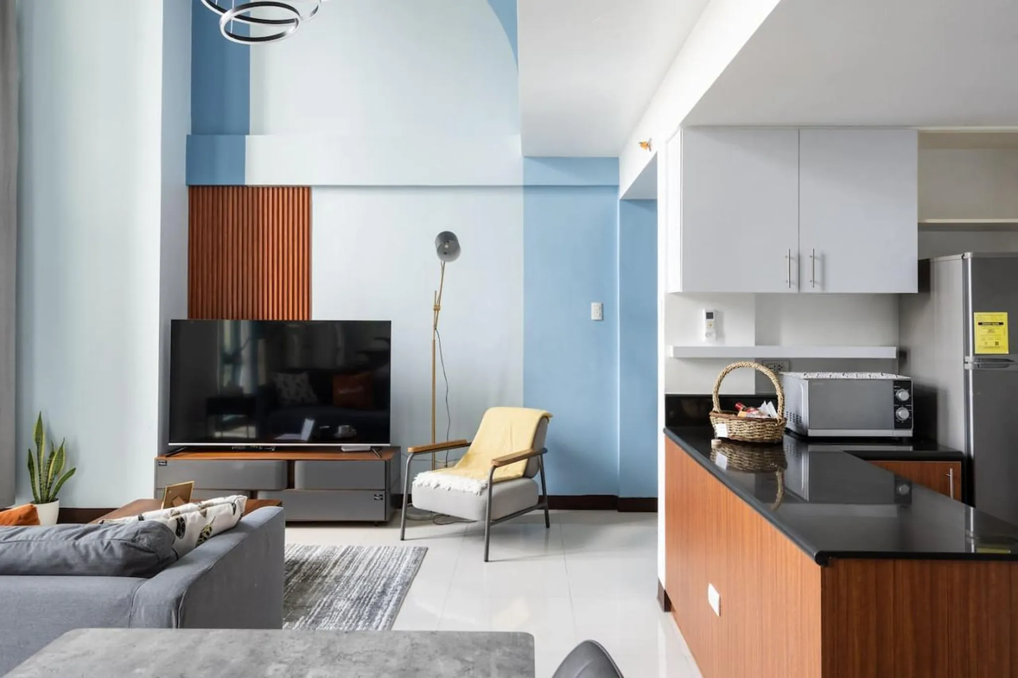 Modern living room and kitchen with blue and white walls, gray sofa, and wooden accents.