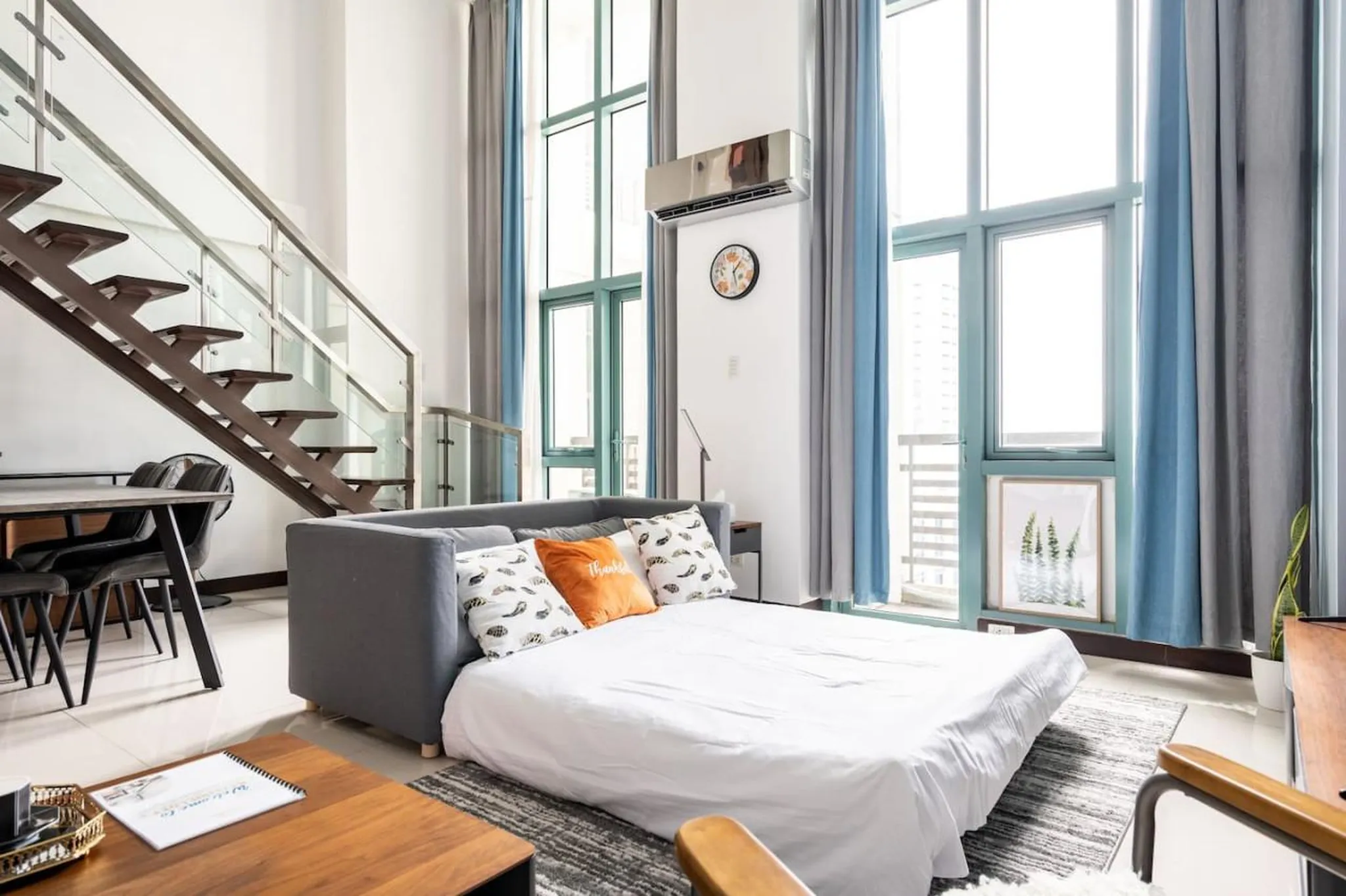 A living room with a sofa bed, a dining table, and a staircase.