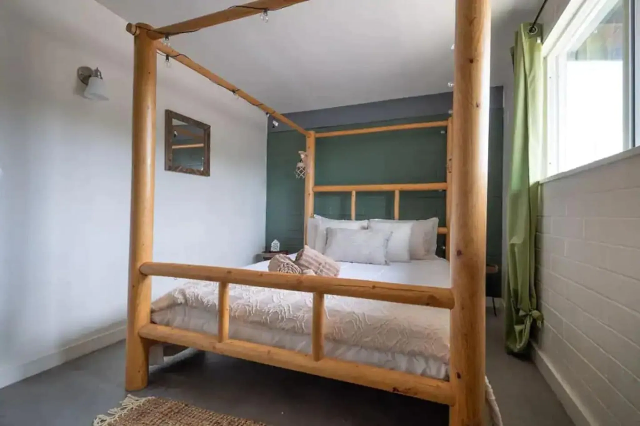 Bedroom with a wooden canopy bed, green accent wall, and large window with green curtains.