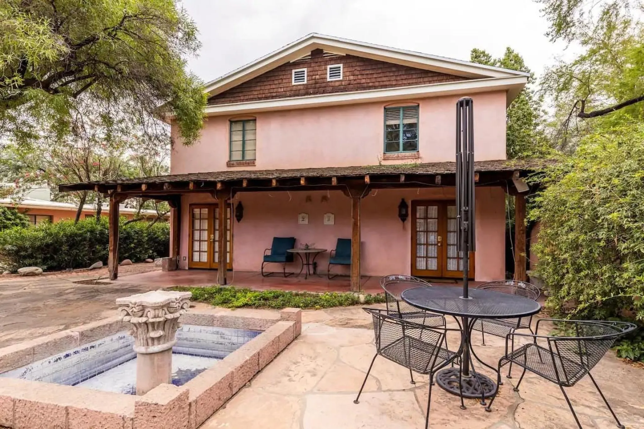 A pink two-story house with a porch, patio, fountain, and outdoor seating.