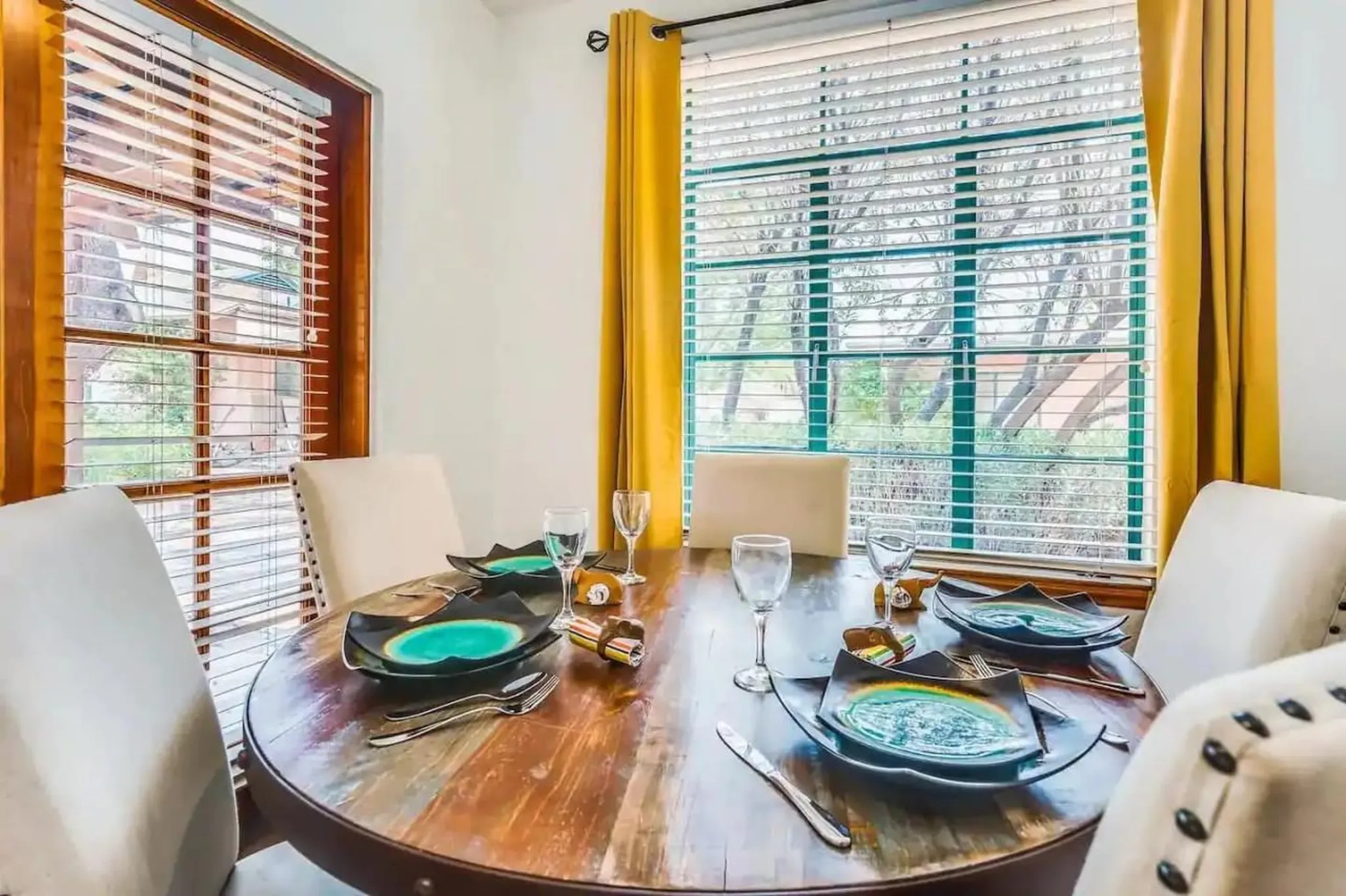 A round wooden dining table is set with plates, glasses, and silverware.