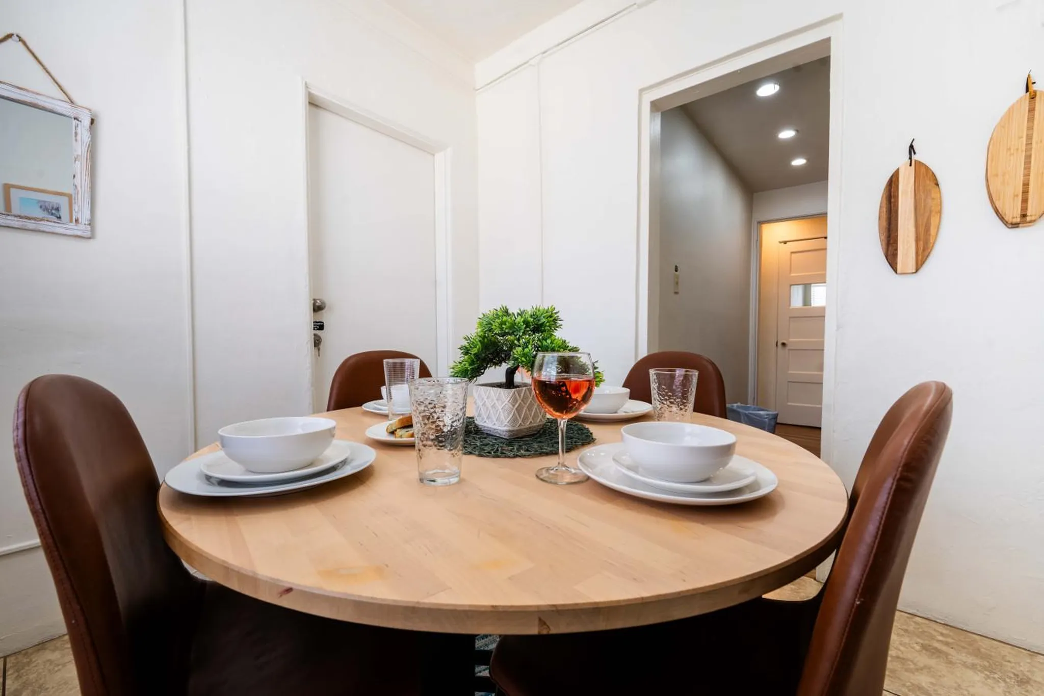 A round wooden table is set with white plates, bowls, and glasses, a glass of rosé, and a small pott