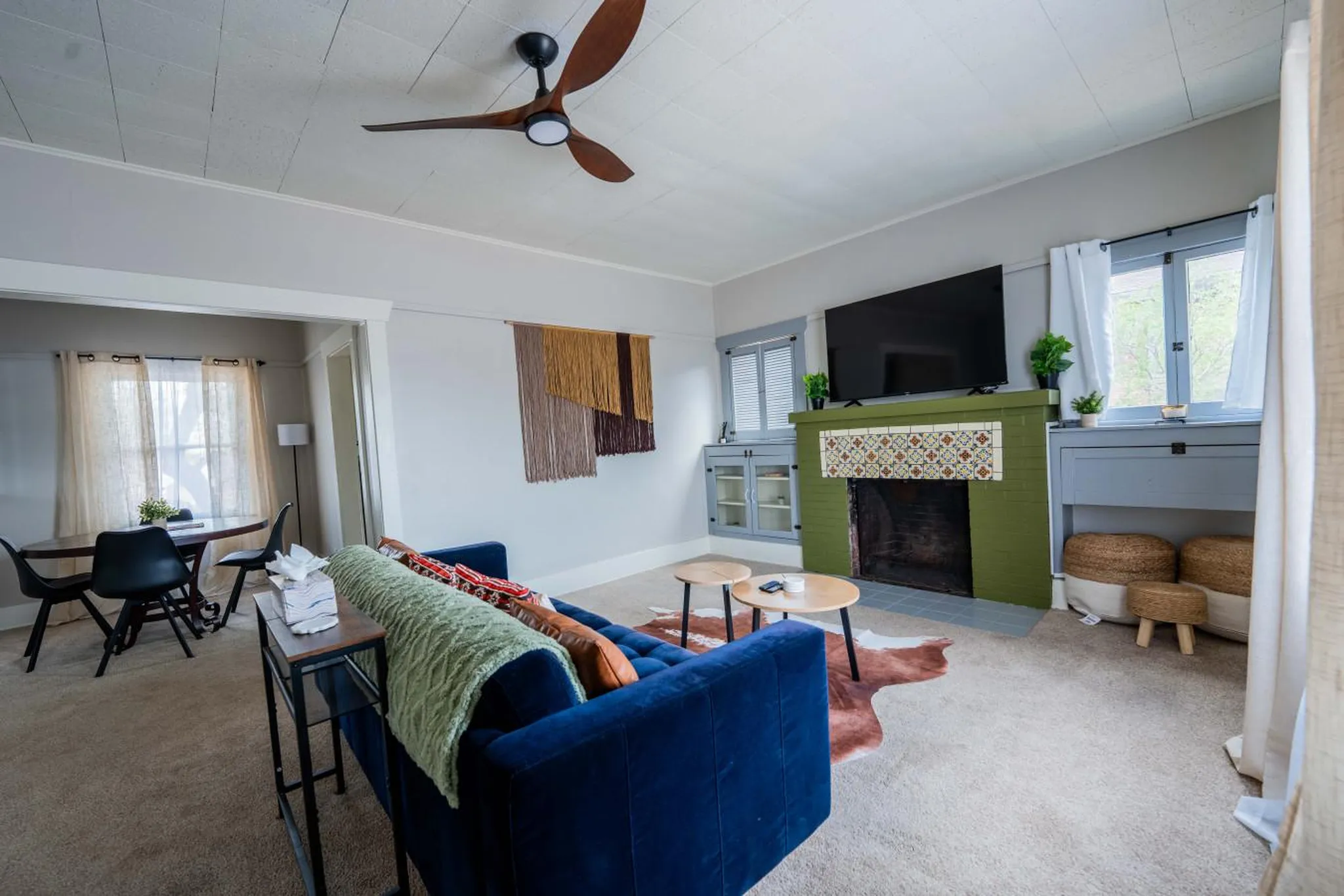 A cozy living room with a blue couch, a green fireplace, and a wooden ceiling fan.