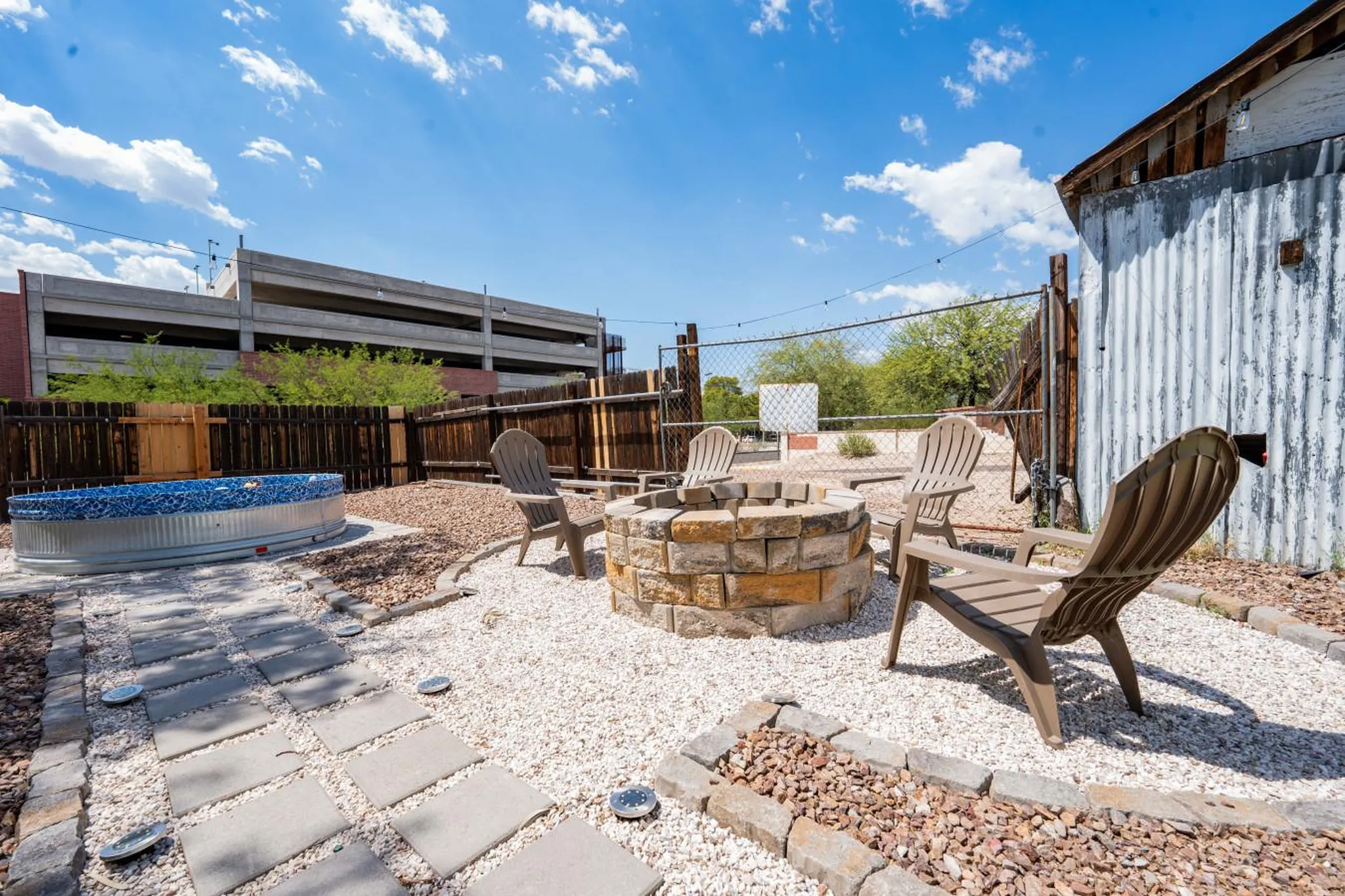 Backyard with a galvanized stock tank pool, fire pit, Adirondack chairs, and corrugated metal shed.