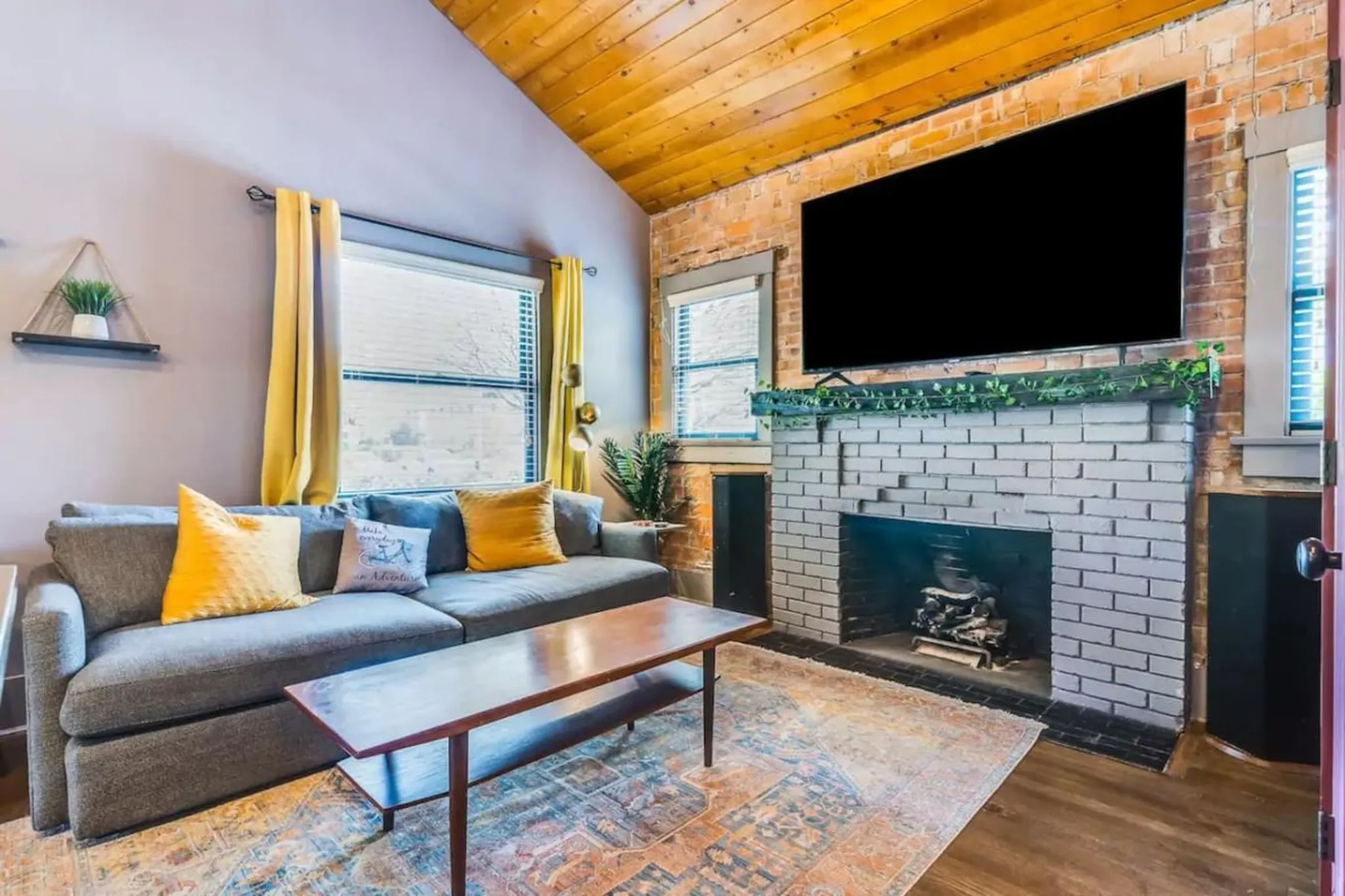 A living room with a grey sectional sofa, yellow accents, a fireplace, and a TV mounted above.