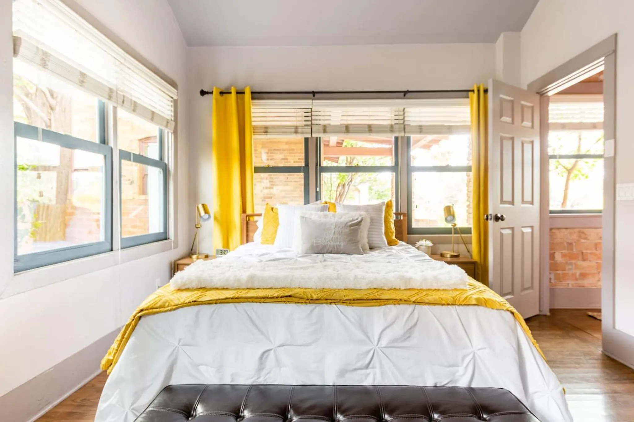 A bright bedroom with a yellow and white comforter, matching curtains, and large windows.