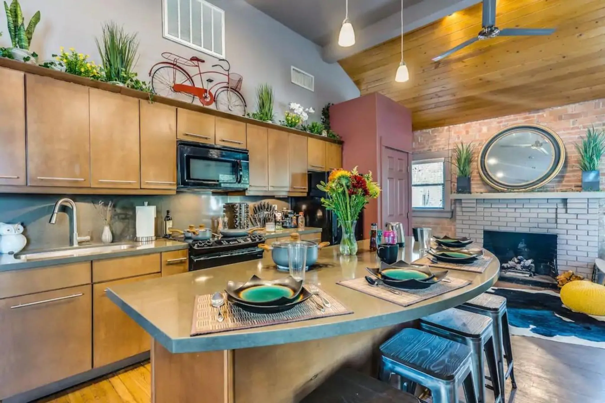 A kitchen with a curved island, brick fireplace, and wooden ceiling.