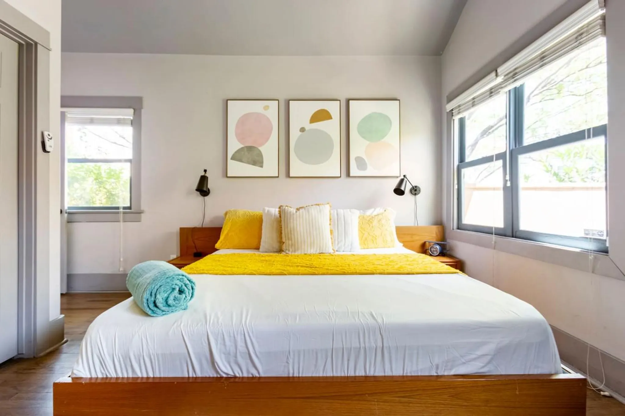 A bed with white sheets and a yellow throw is next to a window.