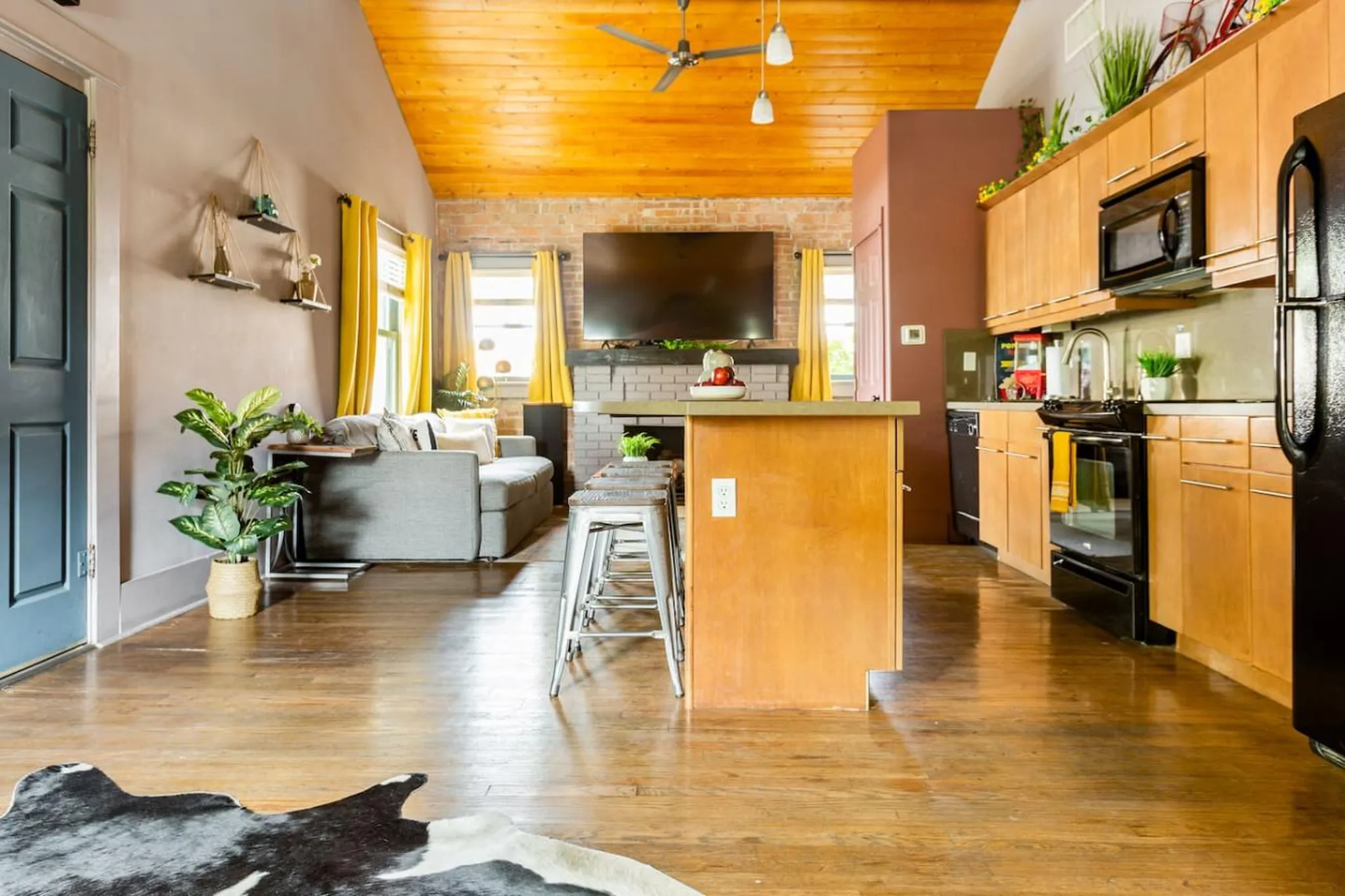 Living room with kitchen island, bar stools, sofa, fireplace, TV, and cowhide rug.