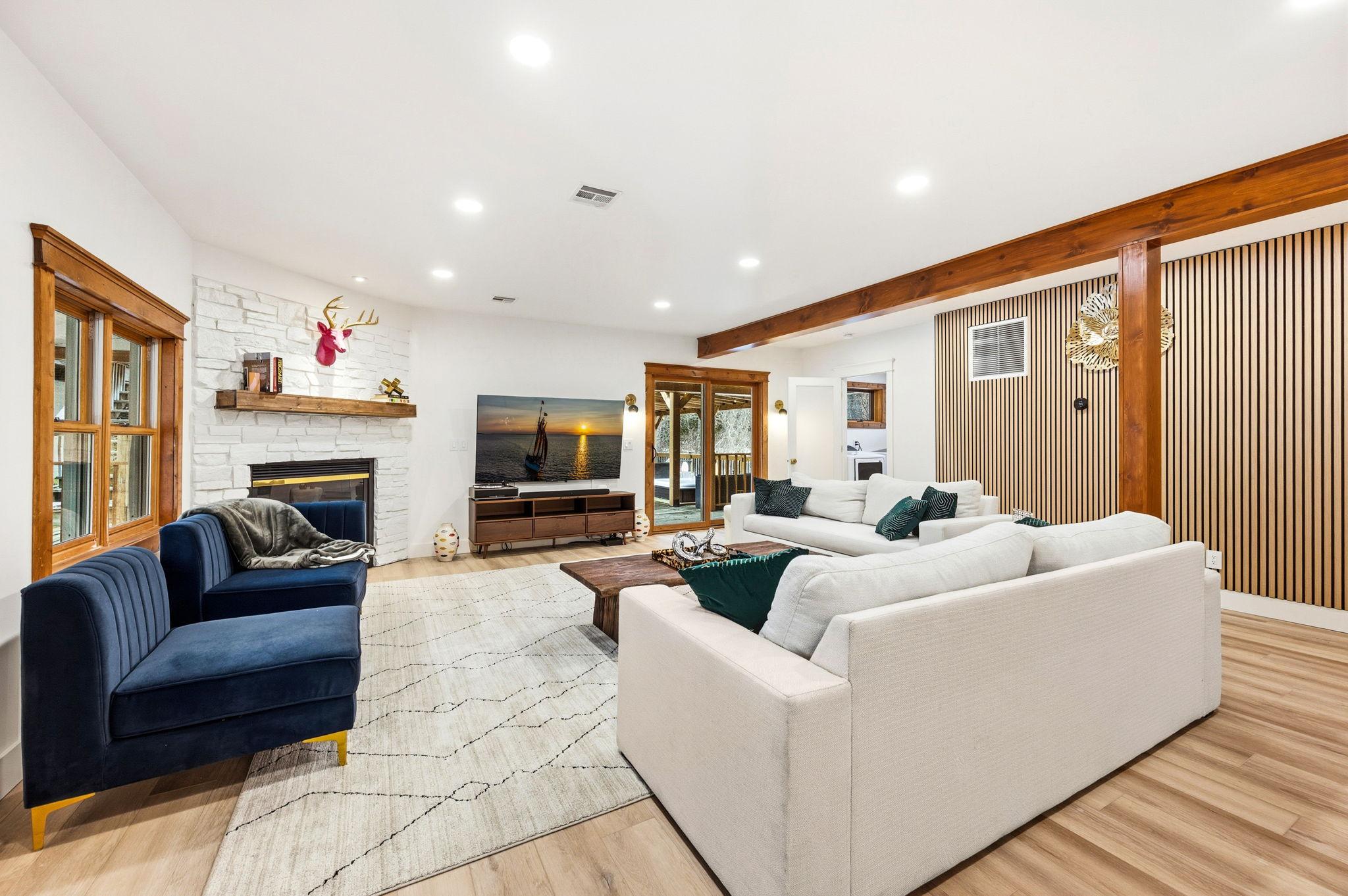 A living room with white walls, a stone fireplace, and wood beams.
