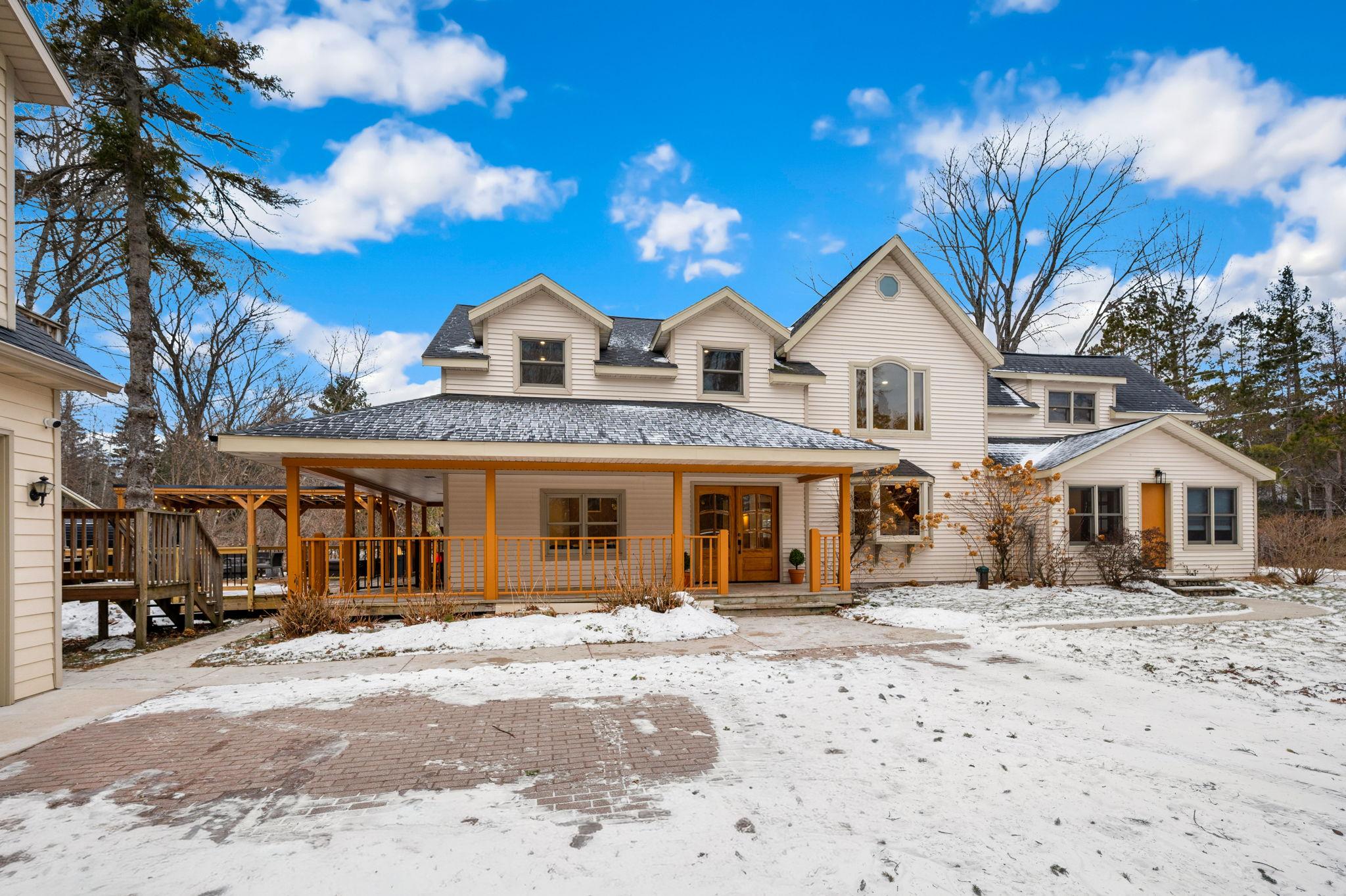 A cream-colored house with a covered porch and a driveway covered in snow.