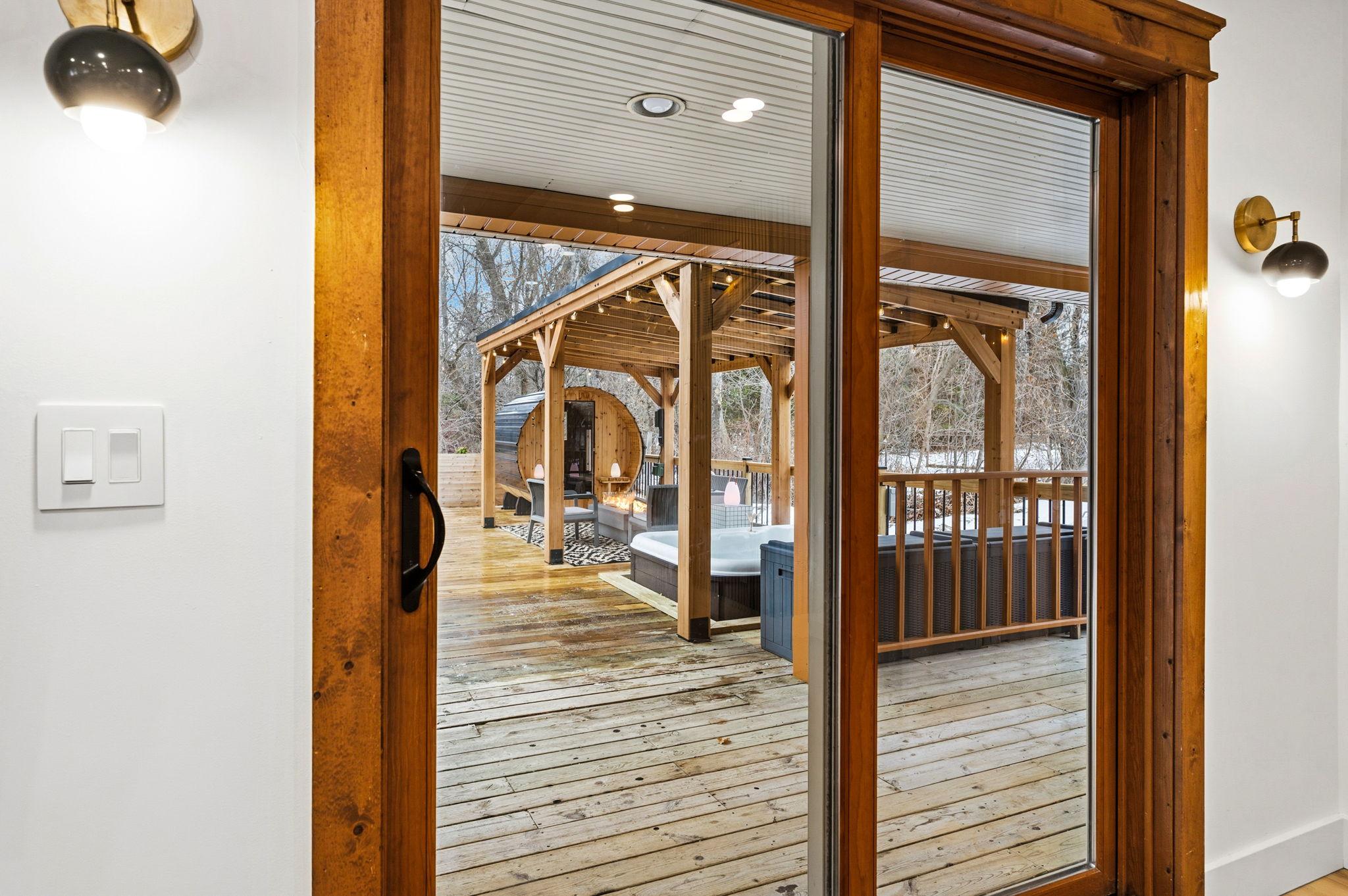 A wooden door with glass panels opens to a backyard deck with a hot tub and a sauna.