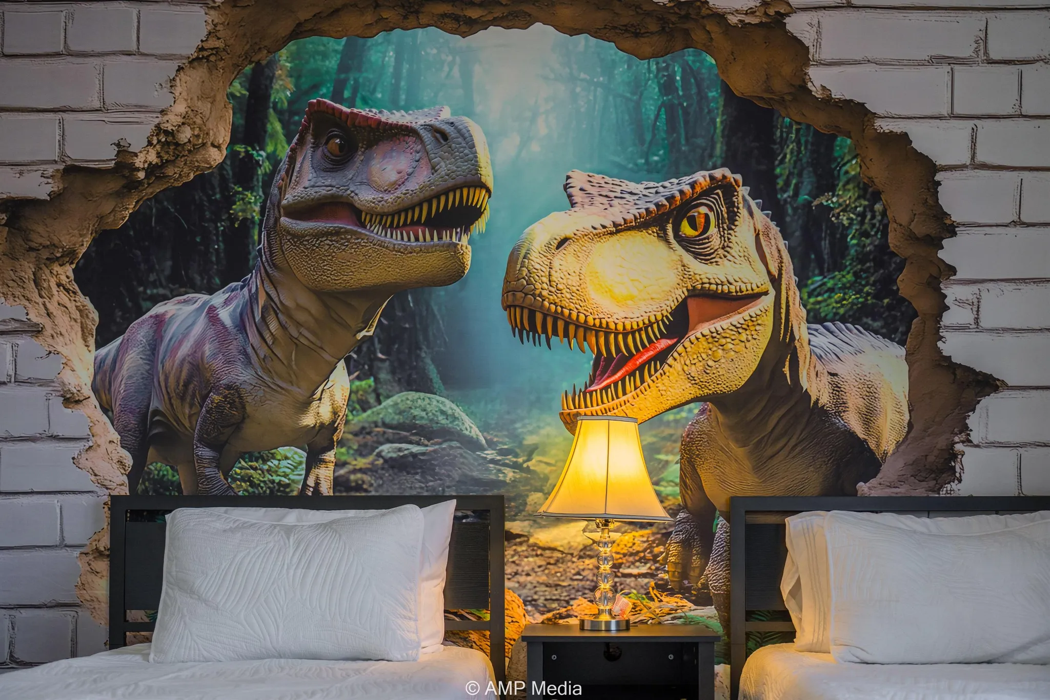 A dinosaur mural is on a wall behind two beds with white pillows.