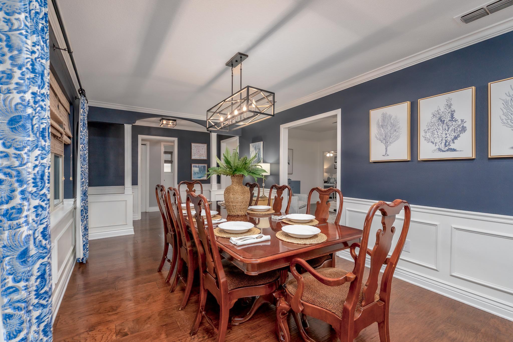 A dining room with a dark blue wall, wainscoting, and a wooden dining table with chairs.