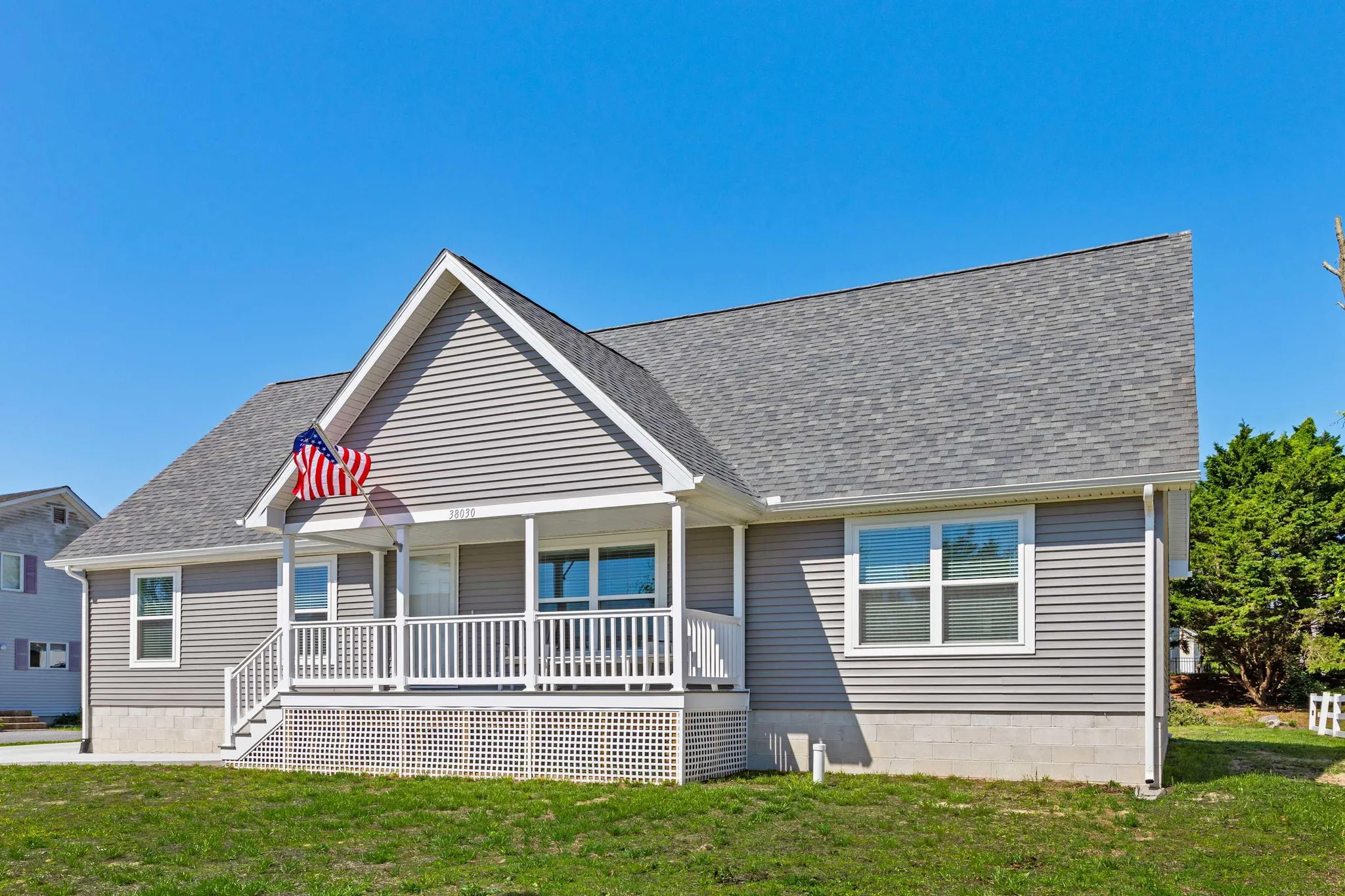 A grey house with a white porch and an American flag.