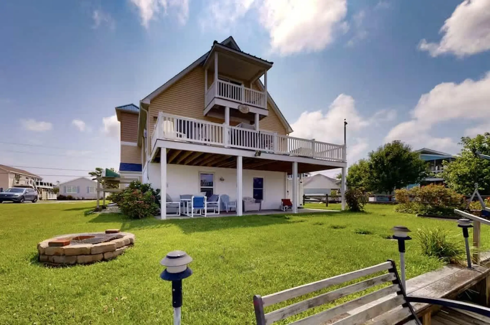 A house with a deck and patio furniture, with a fire pit in the yard.