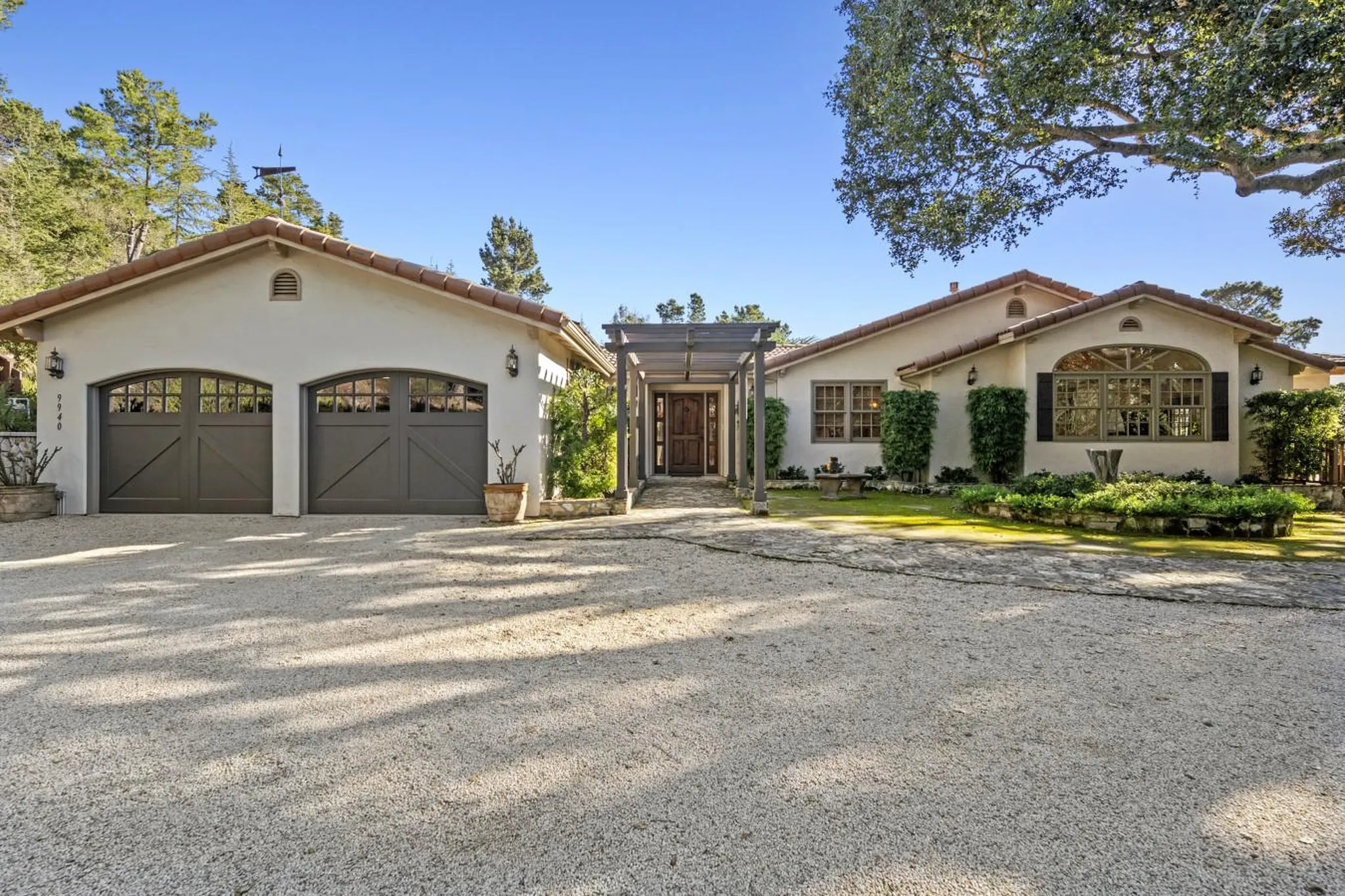 A stucco house with red tile roof has a driveway, garage, and entrance.