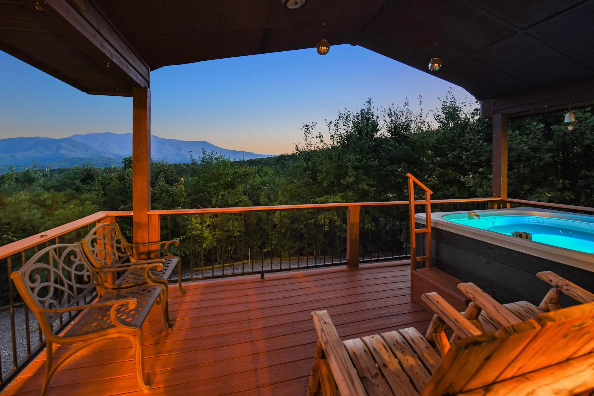 A deck at dusk with a hot tub and mountain view, illuminated by warm lights.