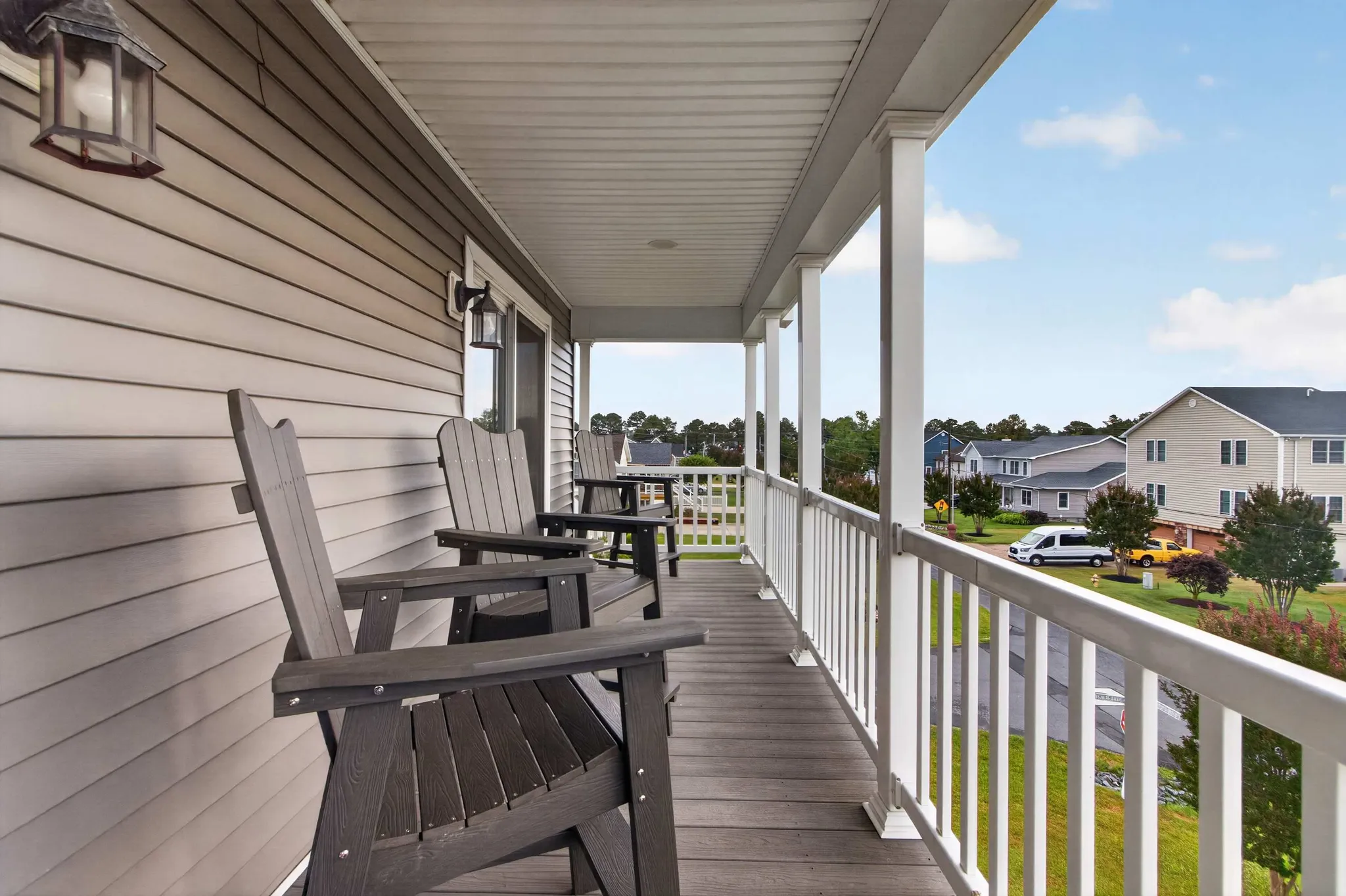 Covered porch with dark Adirondack chairs and white railing overlooking a suburban neighborhood with houses and trees