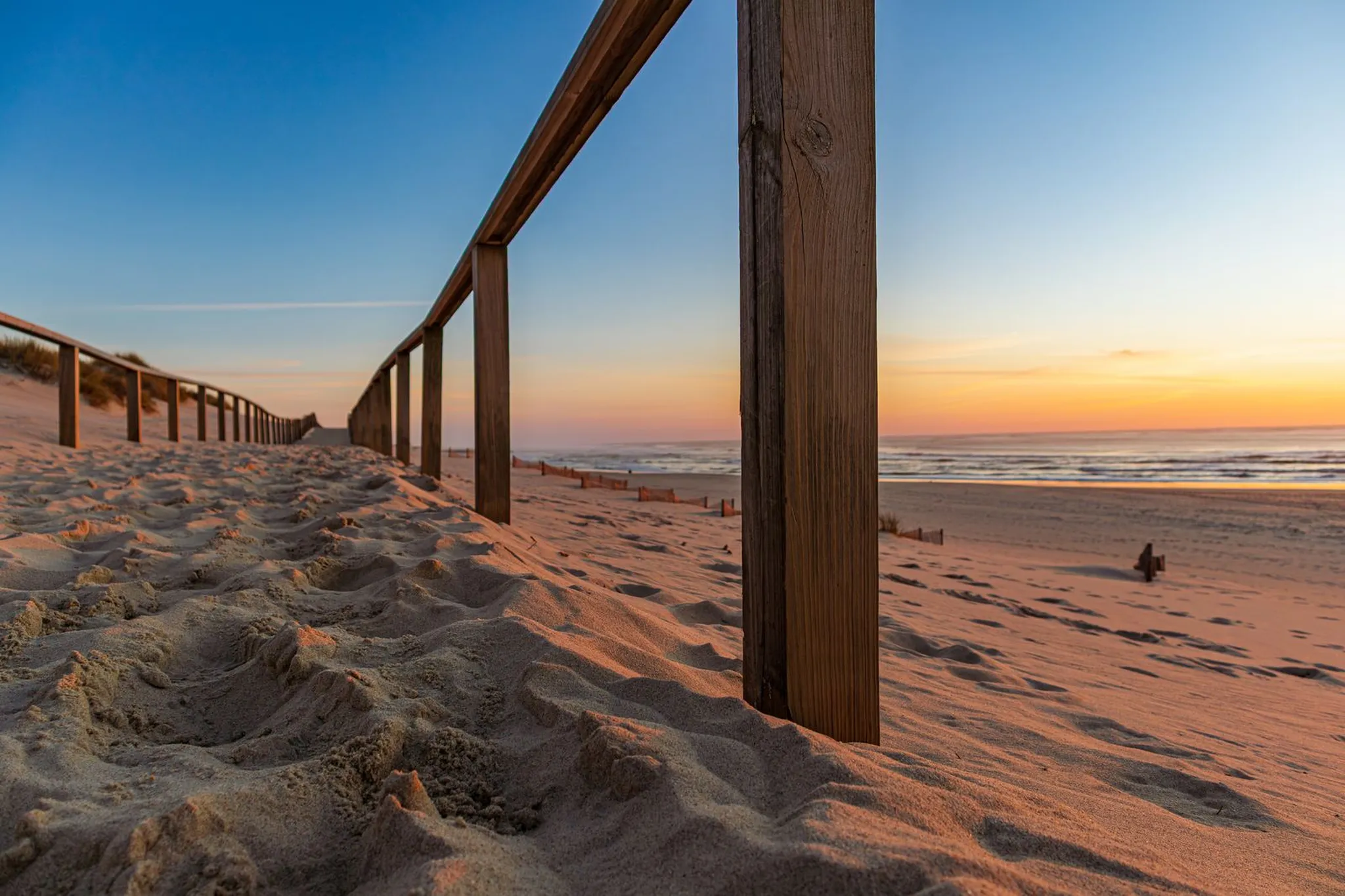 Wooden railing along a sandy beach path at sunrise with the ocean beyond