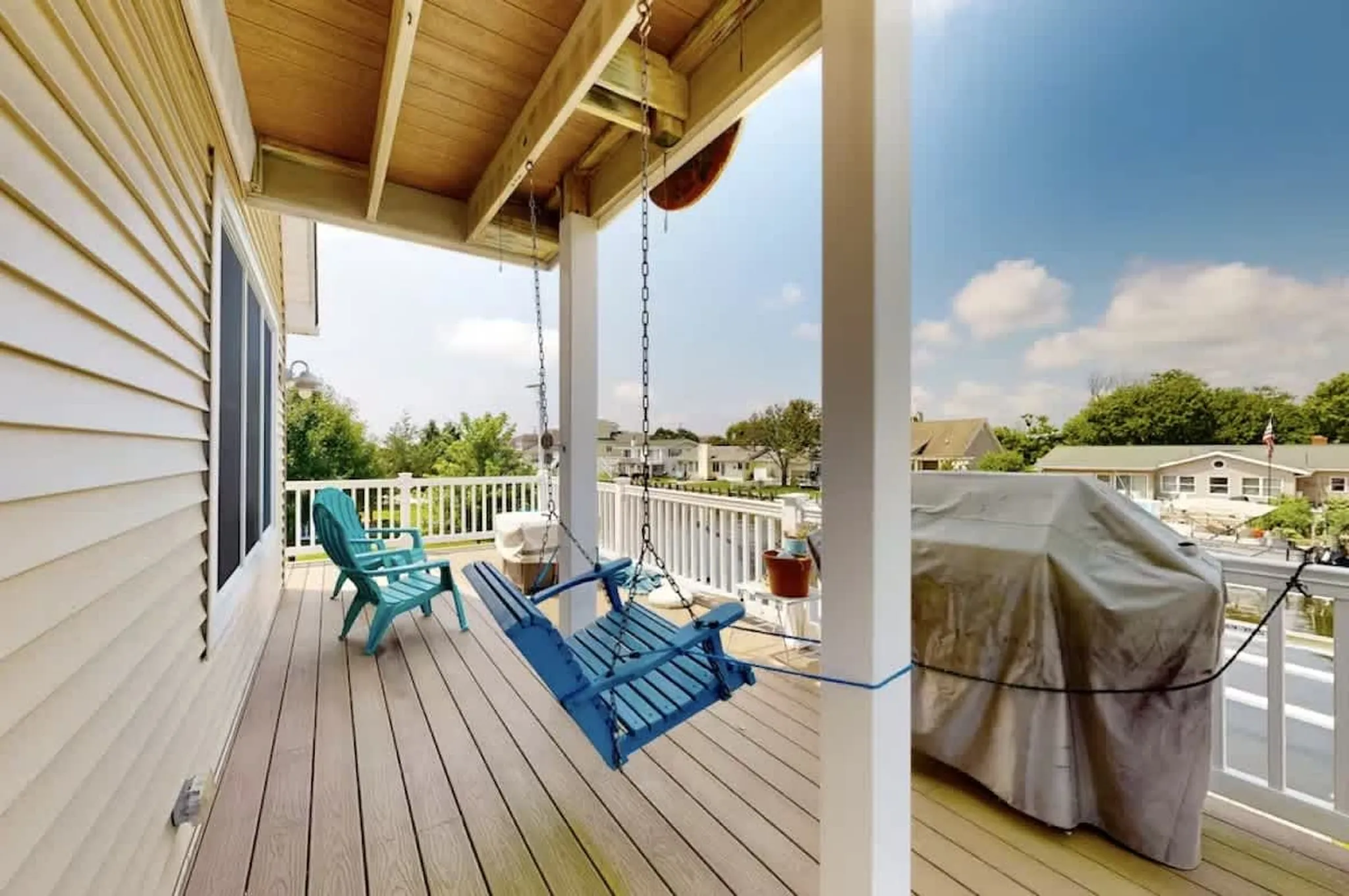 Covered porch with a blue swing bench and Adirondack chair overlooking the neighborhood