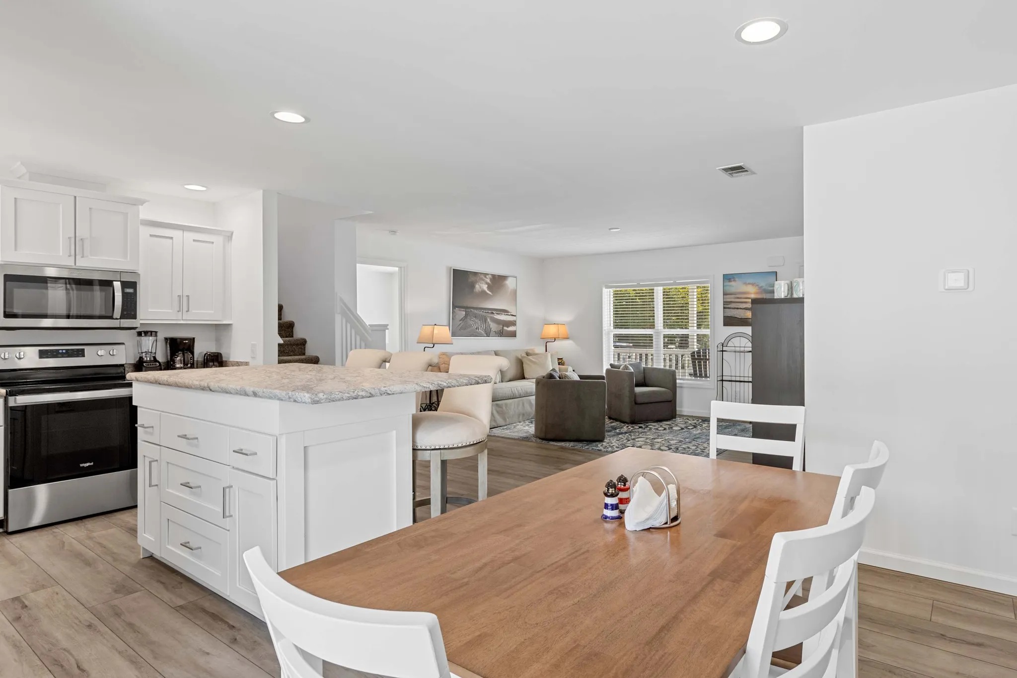 Open-plan kitchen with white cabinets and island, wood dining table, and living room with sofas and armchairs beyond